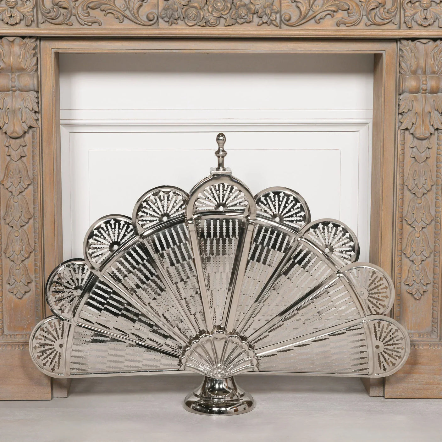 Silver metal firescreen with fan-shaped panels in front of ornate wooden fireplace surround