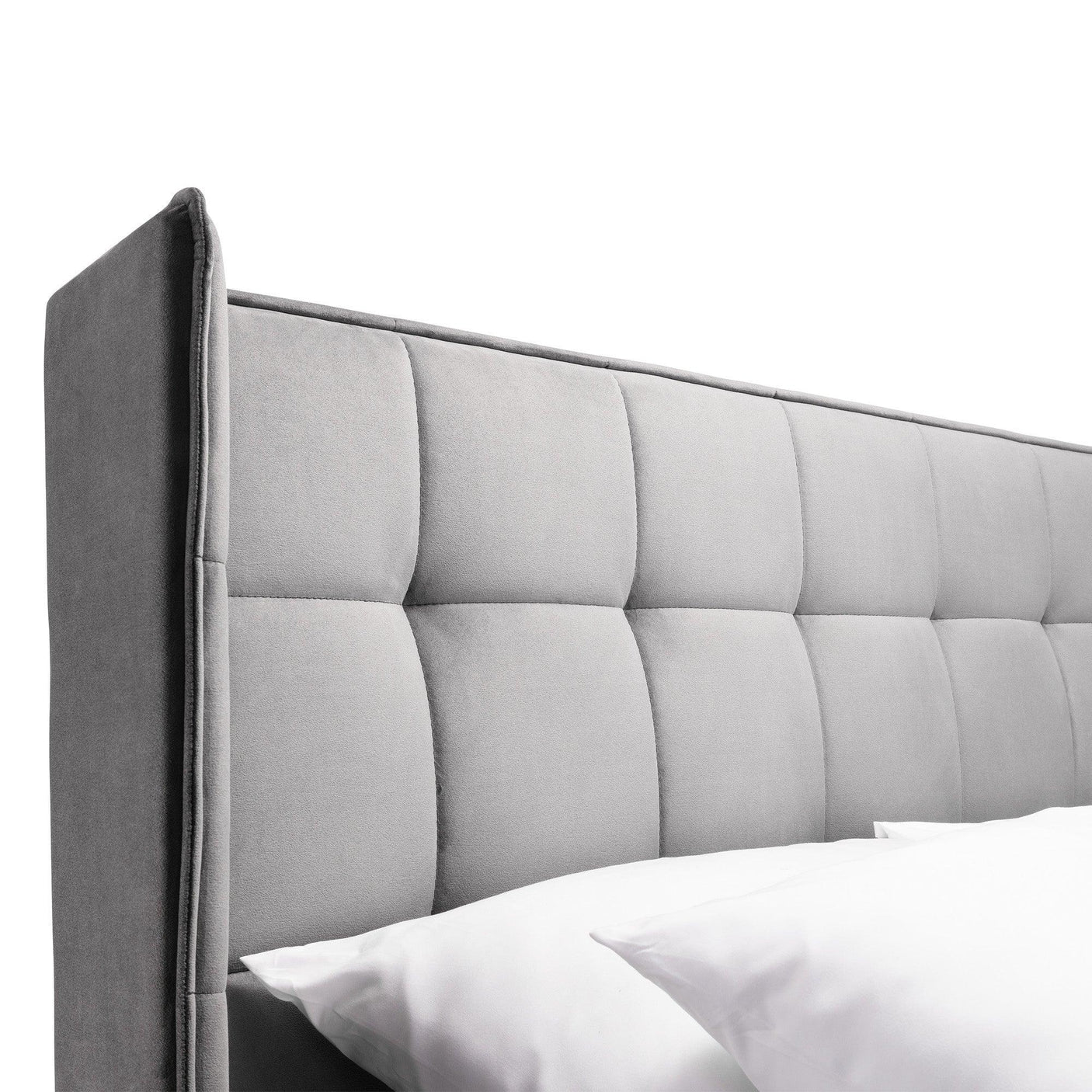 Close up of grey upholstered bed headboard with square stitching and white pillows