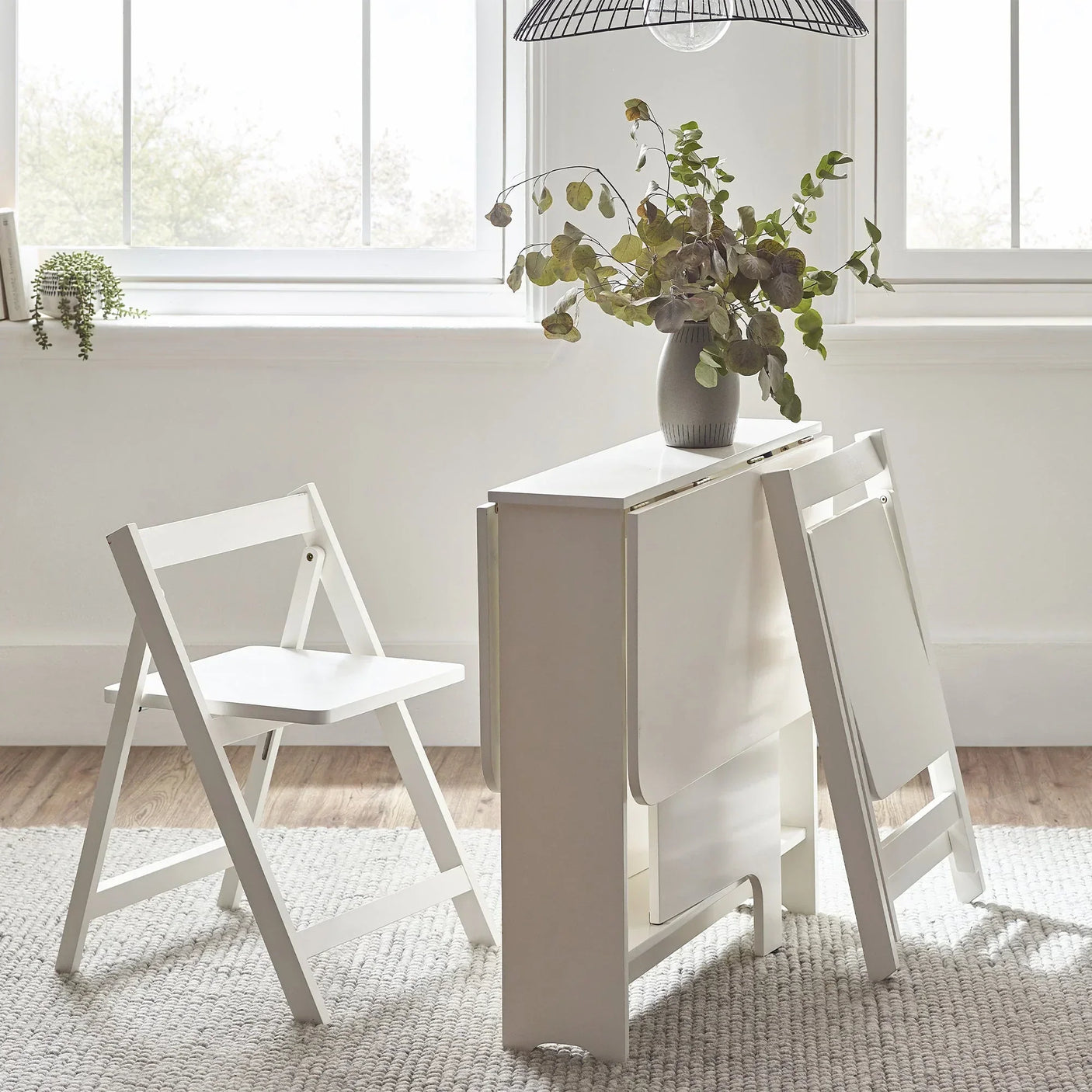 White gateleg table with two folding chairs in bright room, vase with foliage on tabletop