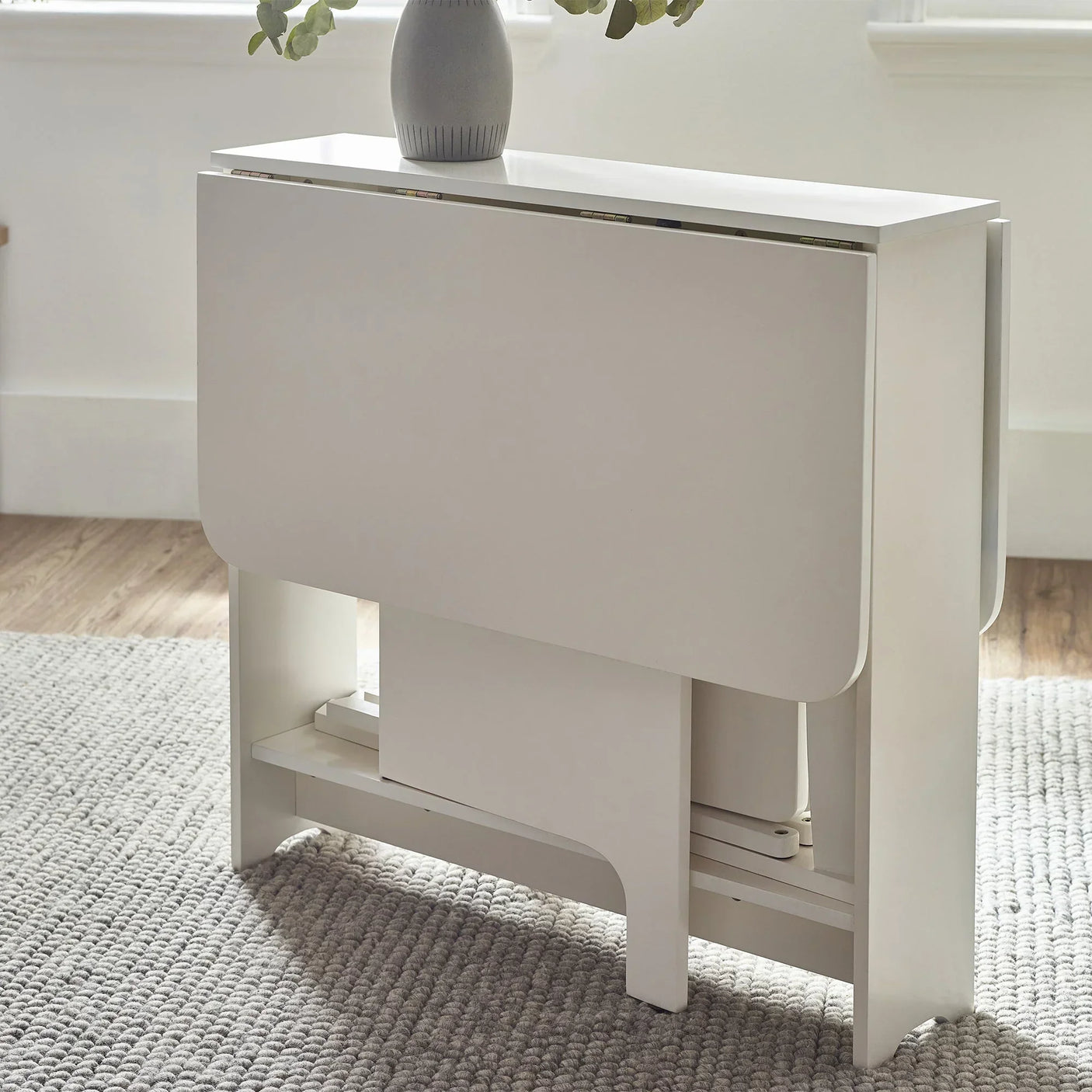 White gateleg dining table with folded leaves in bright room on textured rug