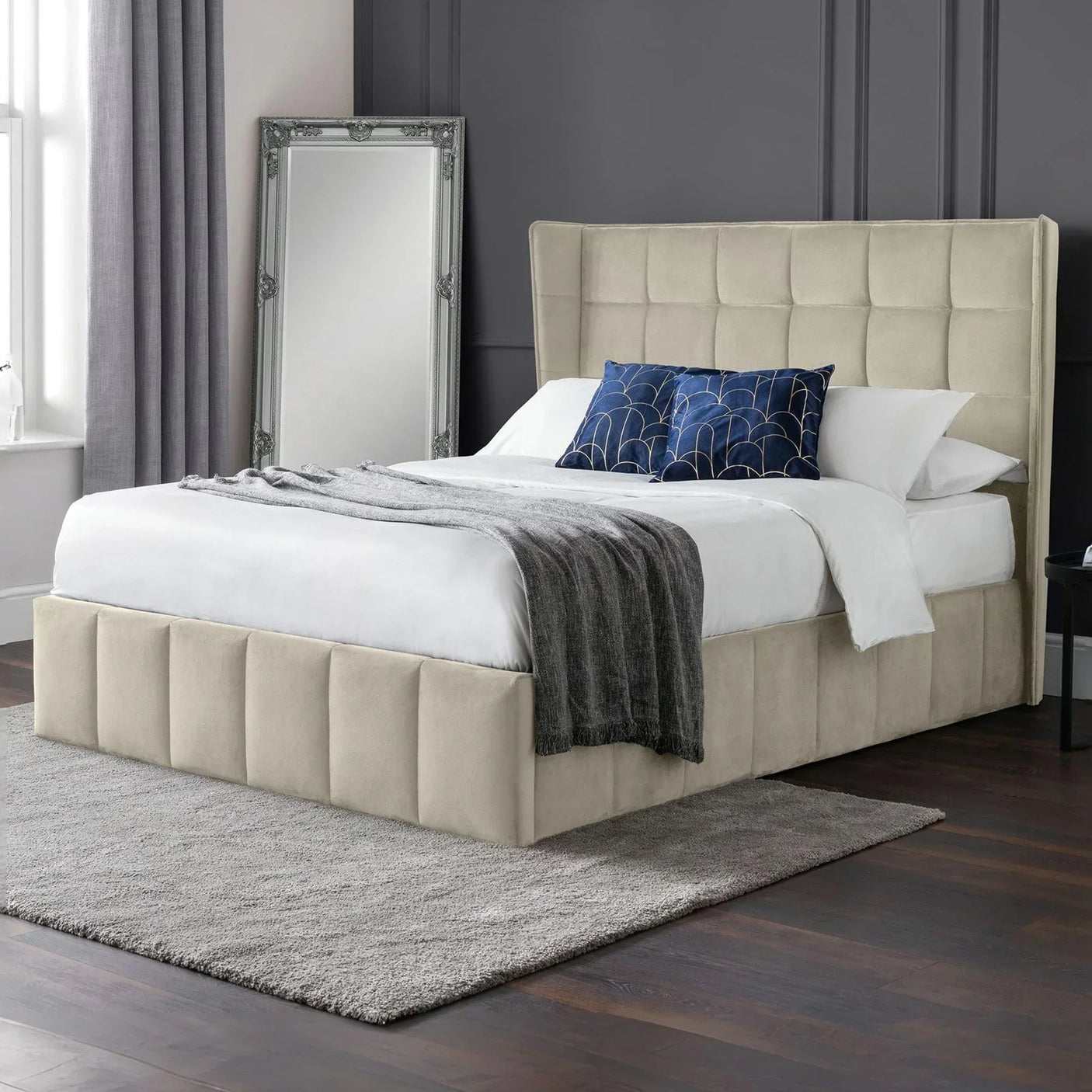 Beige upholstered bed with tall headboard, white bedding, and blue cushions in a modern bedroom