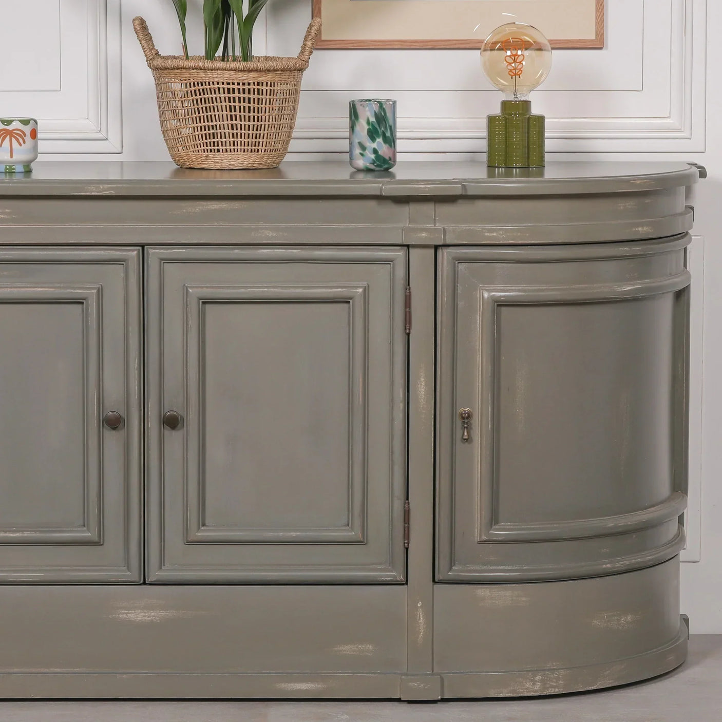 Grey painted sideboard cabinet with paneled doors and curved edges against white wall