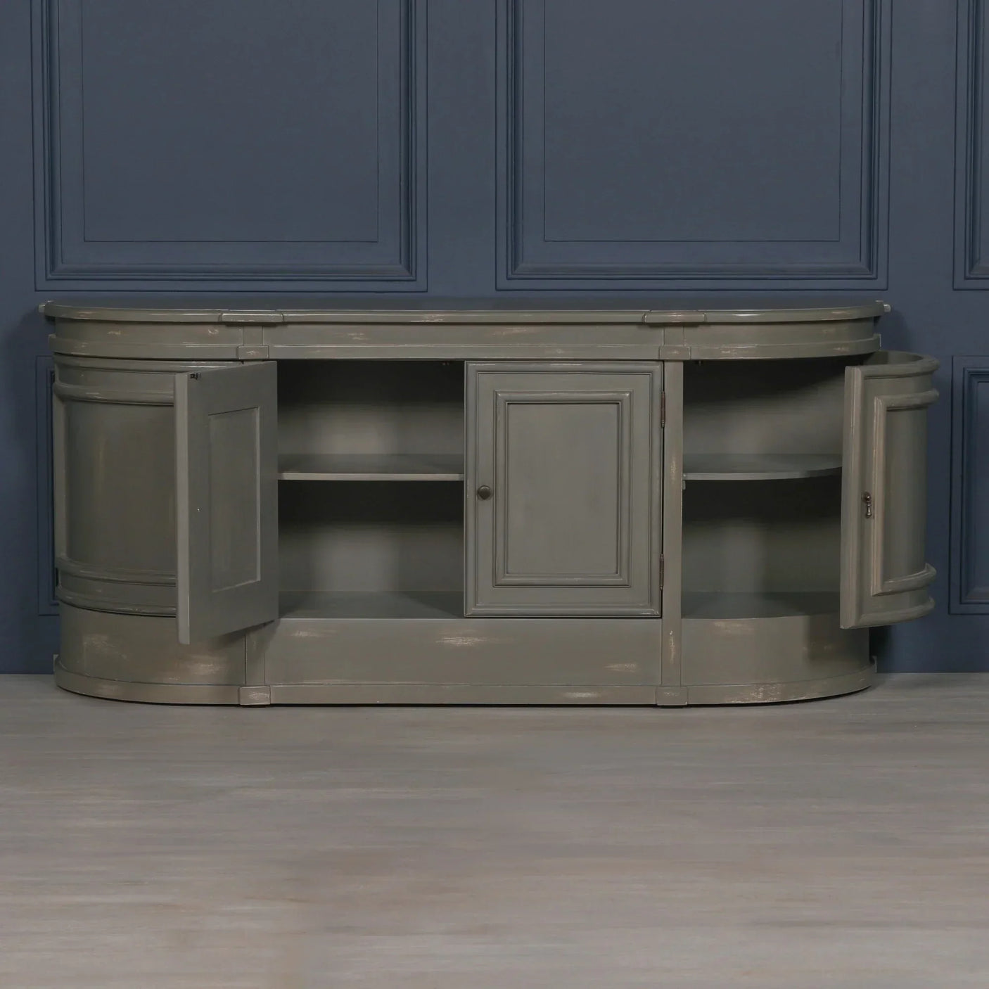 Grey wooden sideboard with three open storage cabinets against blue panel wall