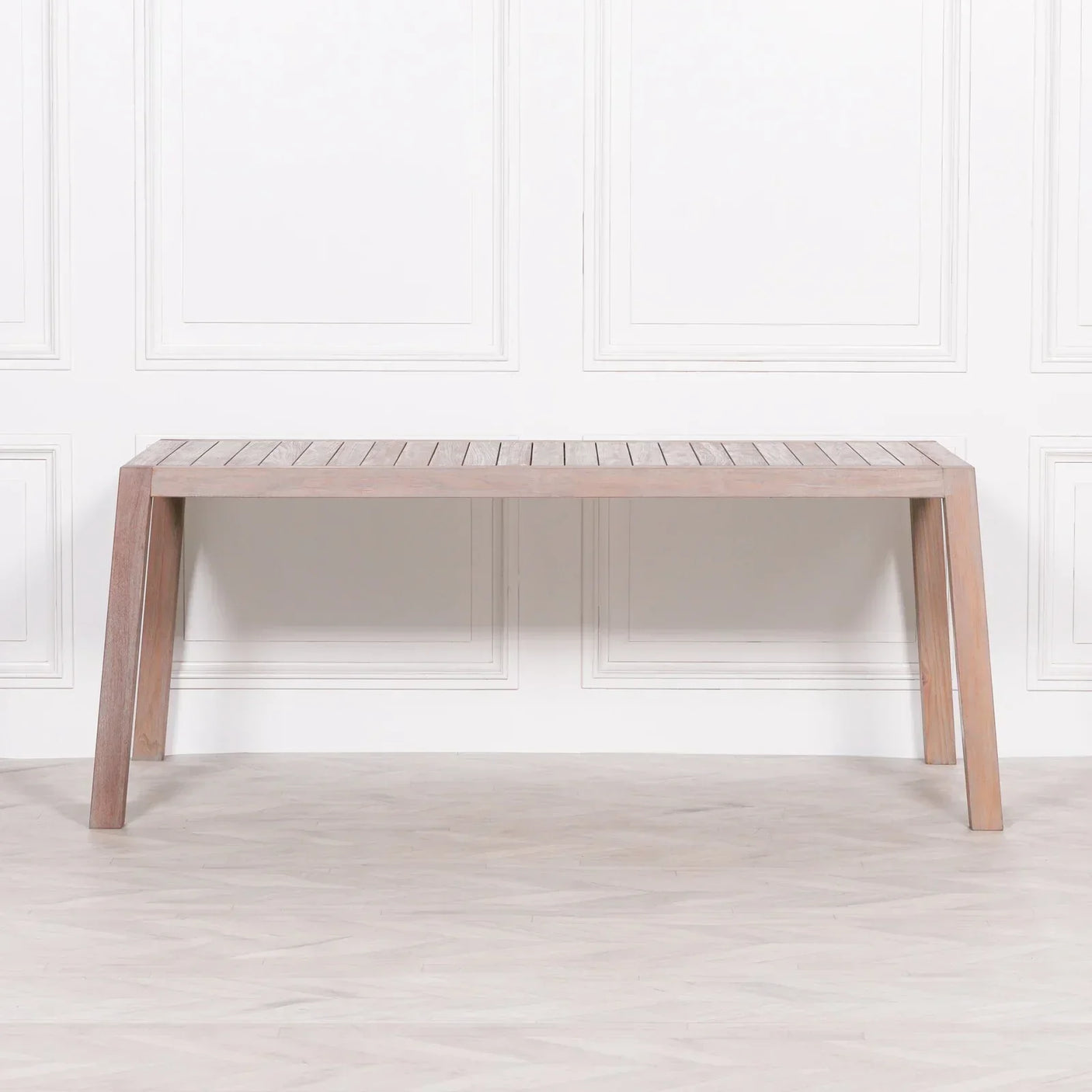 Rectangular wooden dining table with slatted top and angled legs against white wall