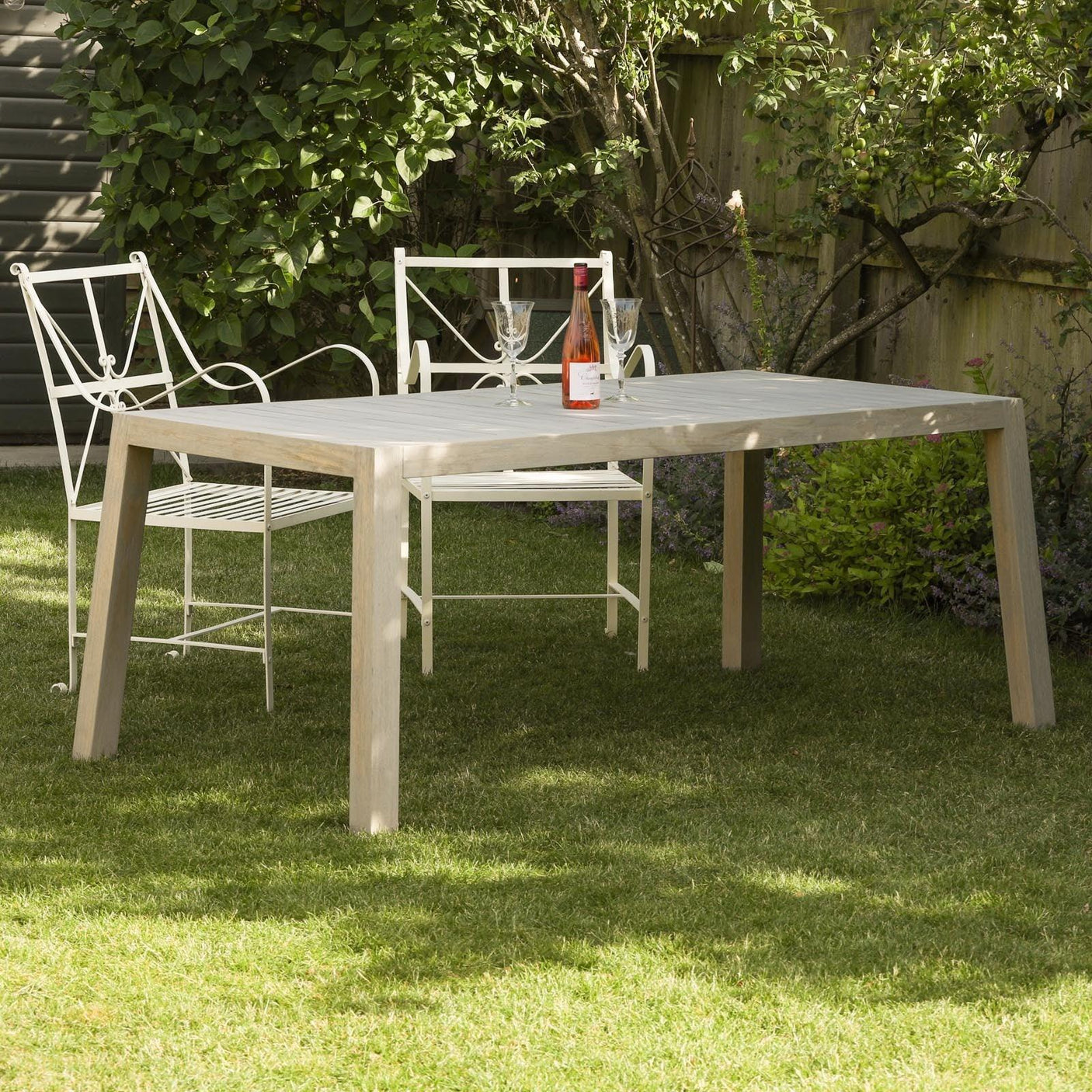 Rectangular outdoor dining table with wood finish and metal chairs set on grass garden