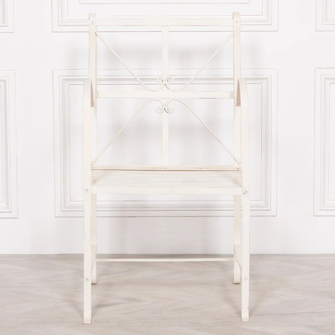 White metal garden bench with decorative scrollwork backrest against panelled wall