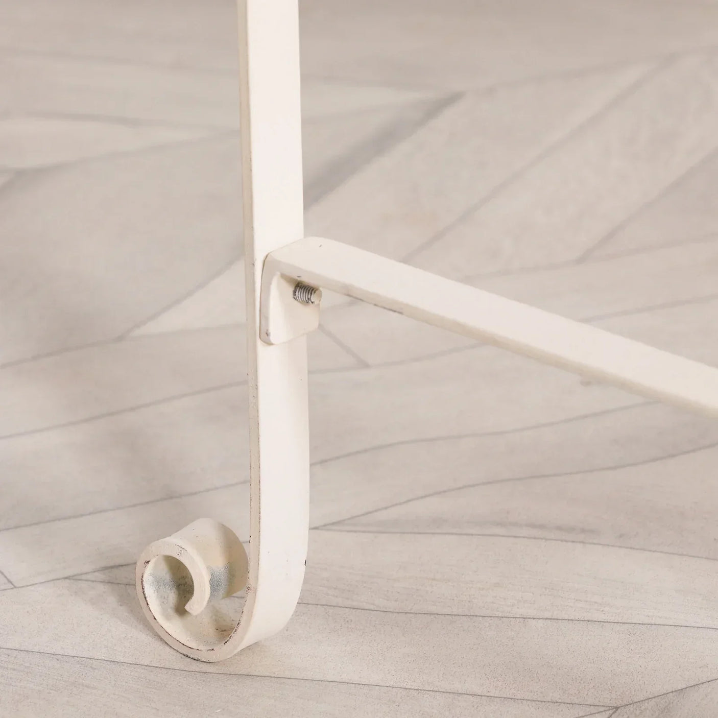 Cream metal furniture leg with curled scroll detail on light wood floor