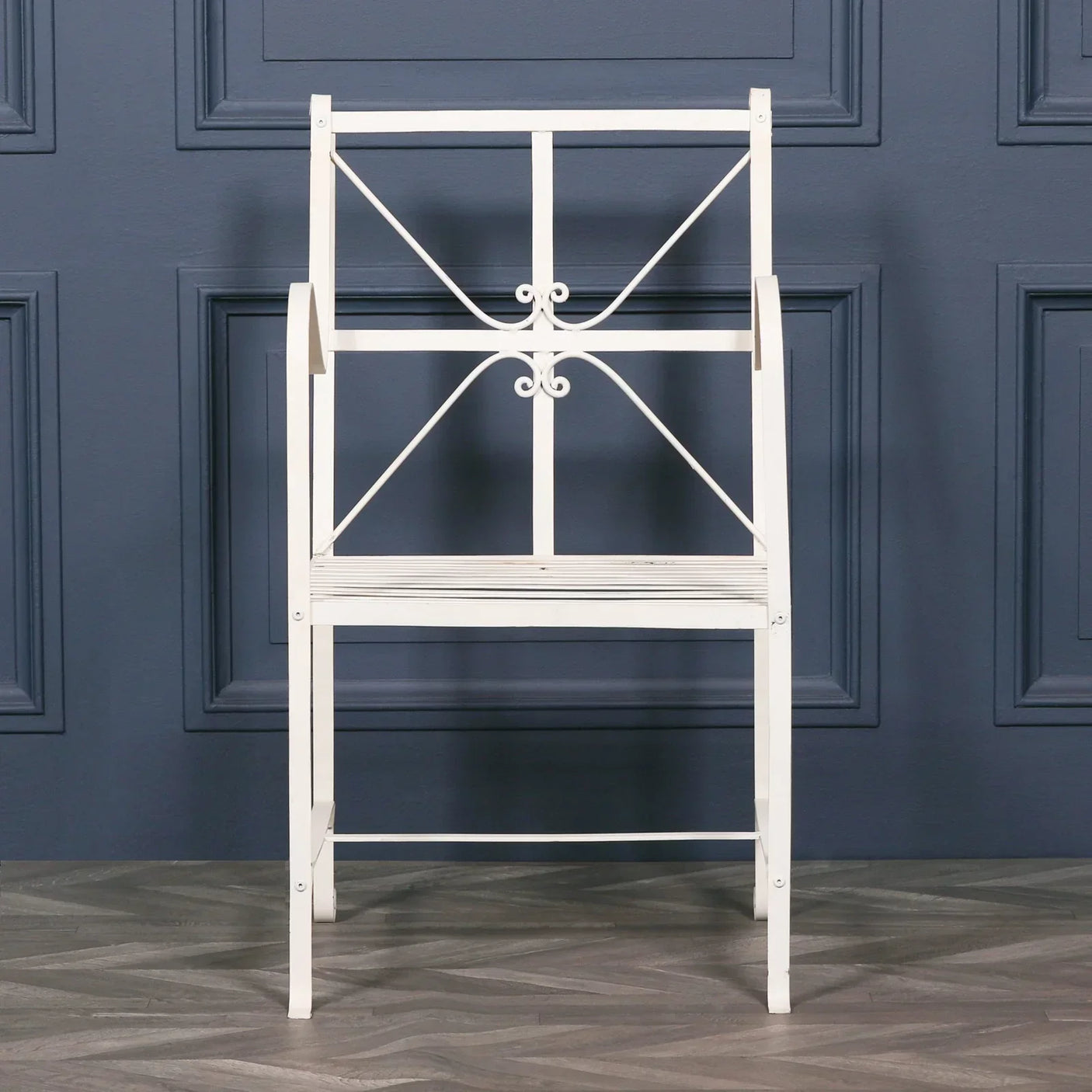 White metal garden bench with decorative scroll backrest against blue paneled wall