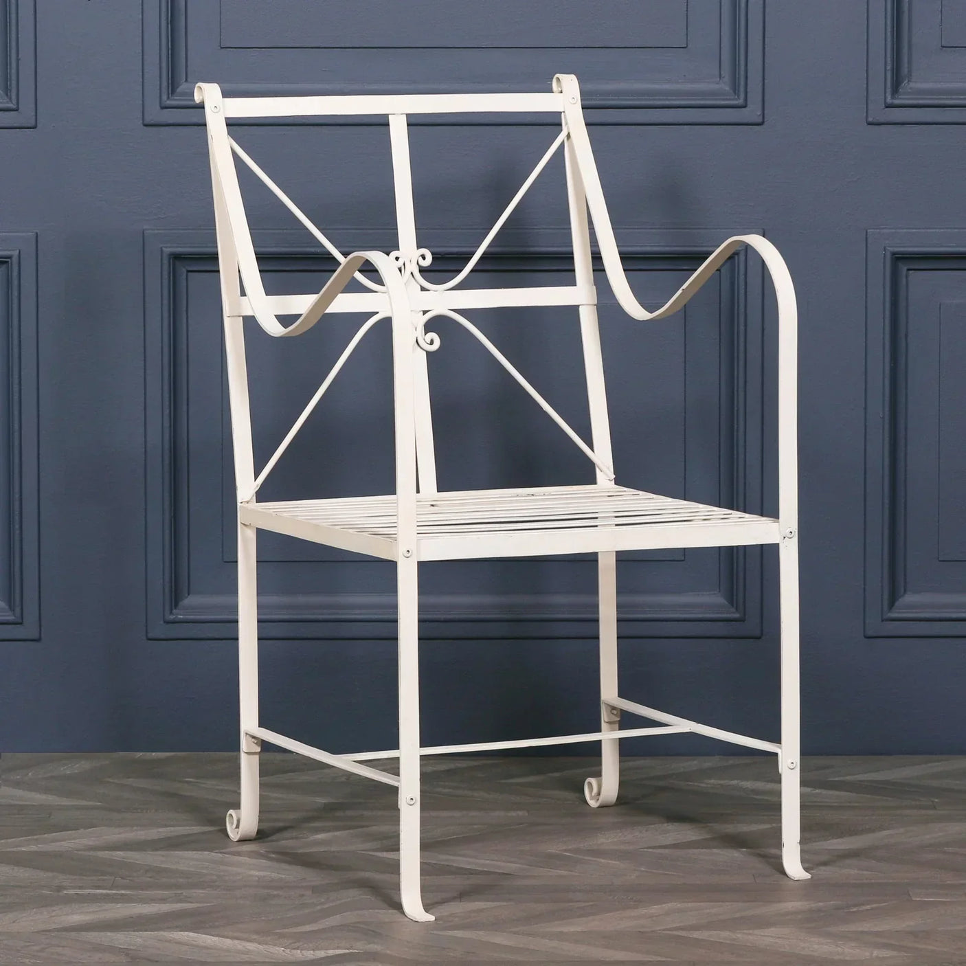 White metal garden chair with decorative scroll arms and slatted seat on wood floor