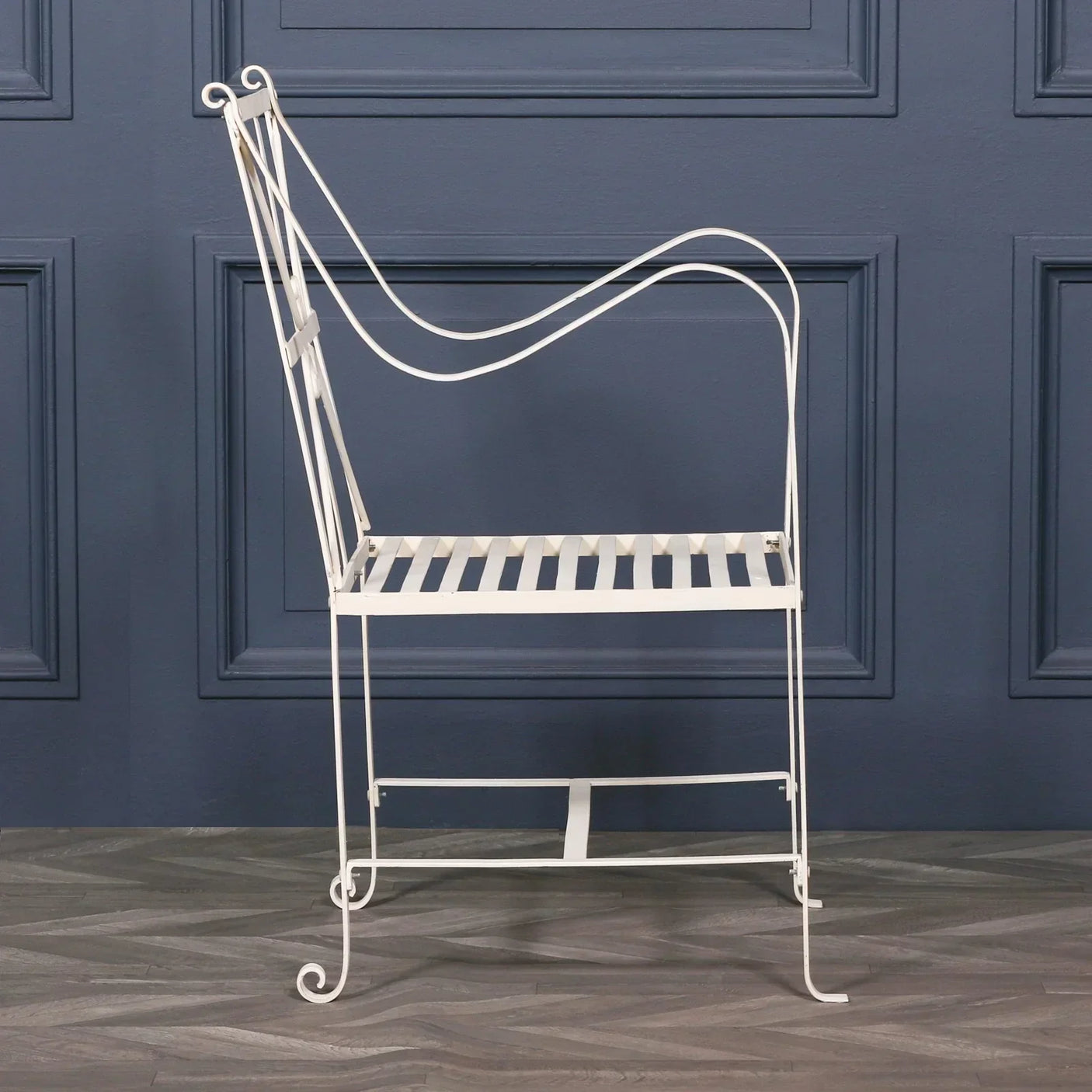 White metal garden chair with decorative armrests against a navy blue wall