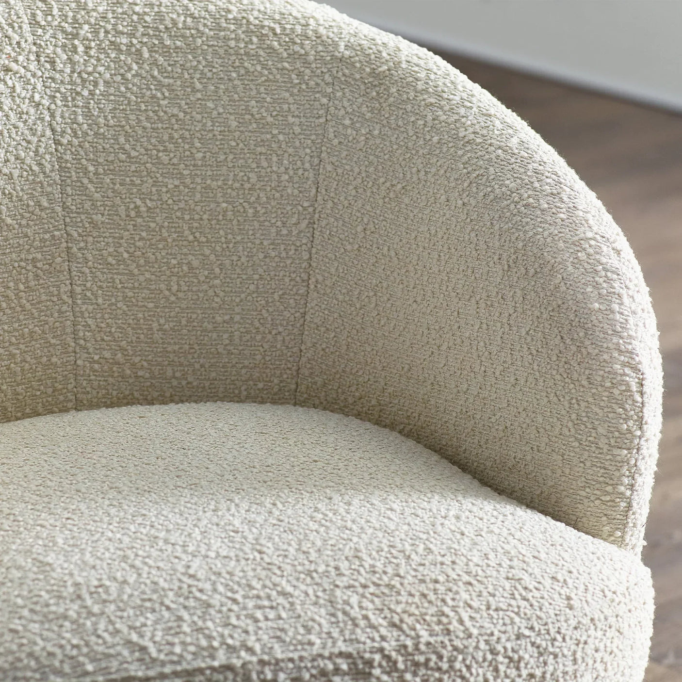 Closeup of cream boucle accent chair upholstery and curved backrest on wood floor