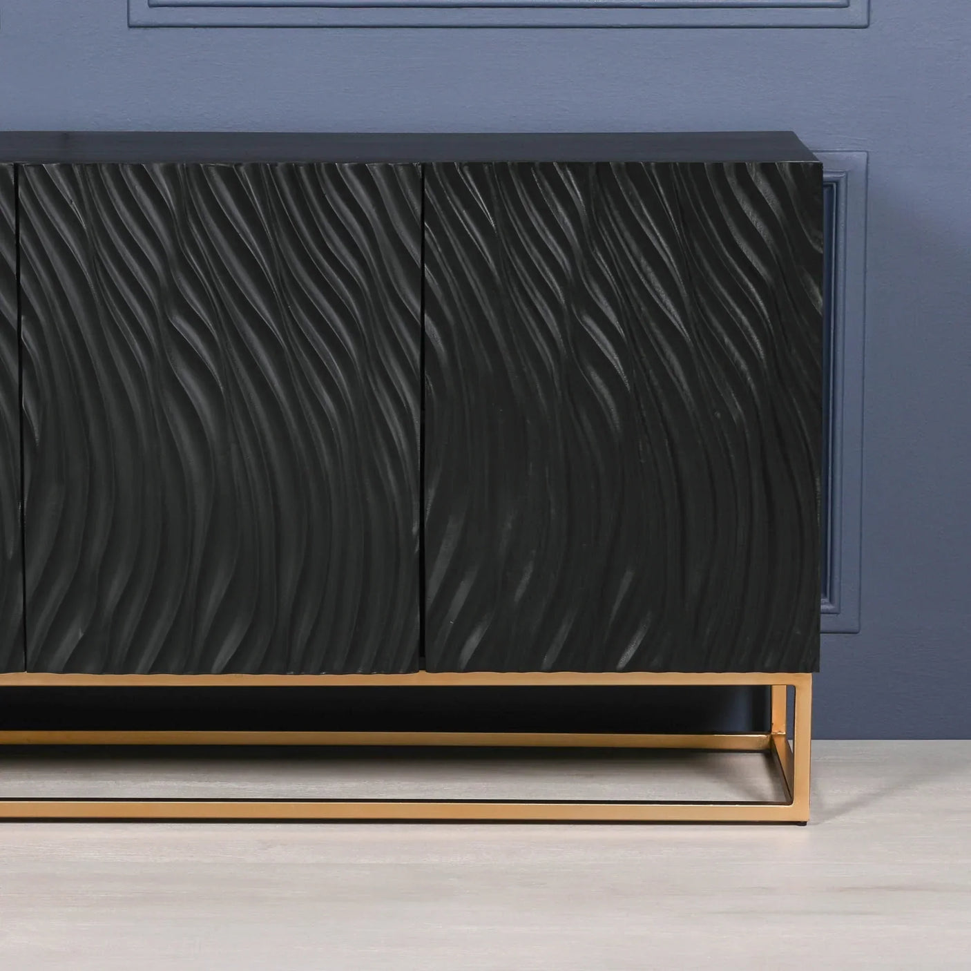 Black sideboard with textured wavy doors and gold metal base against blue wall