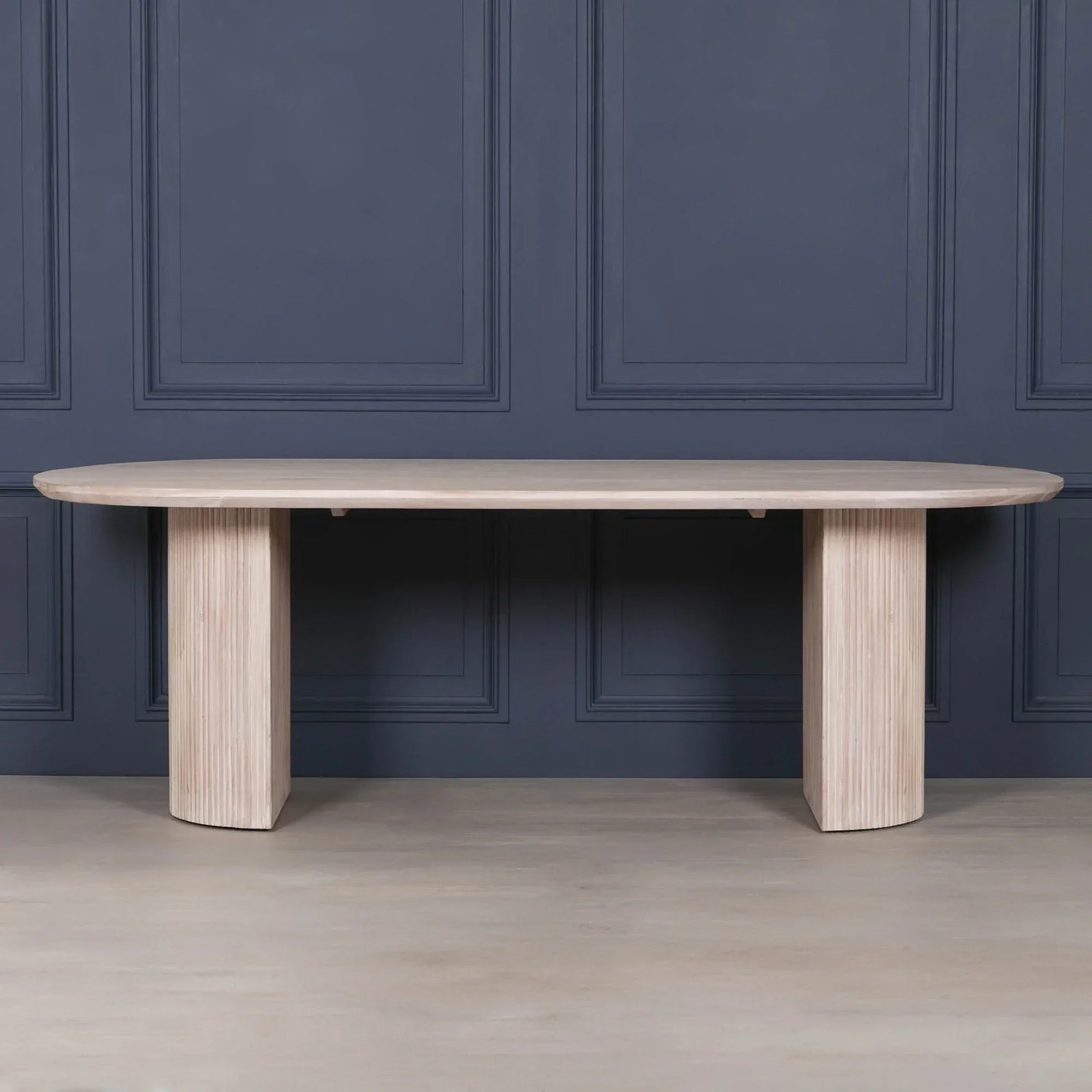 Rectangular oak dining table with fluted pedestal legs against dark panelled wall