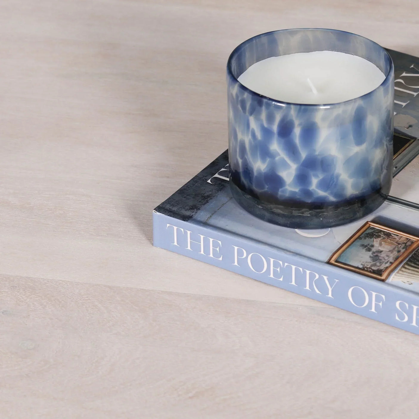 Blue glass candle holder with white candle on book atop light wood table