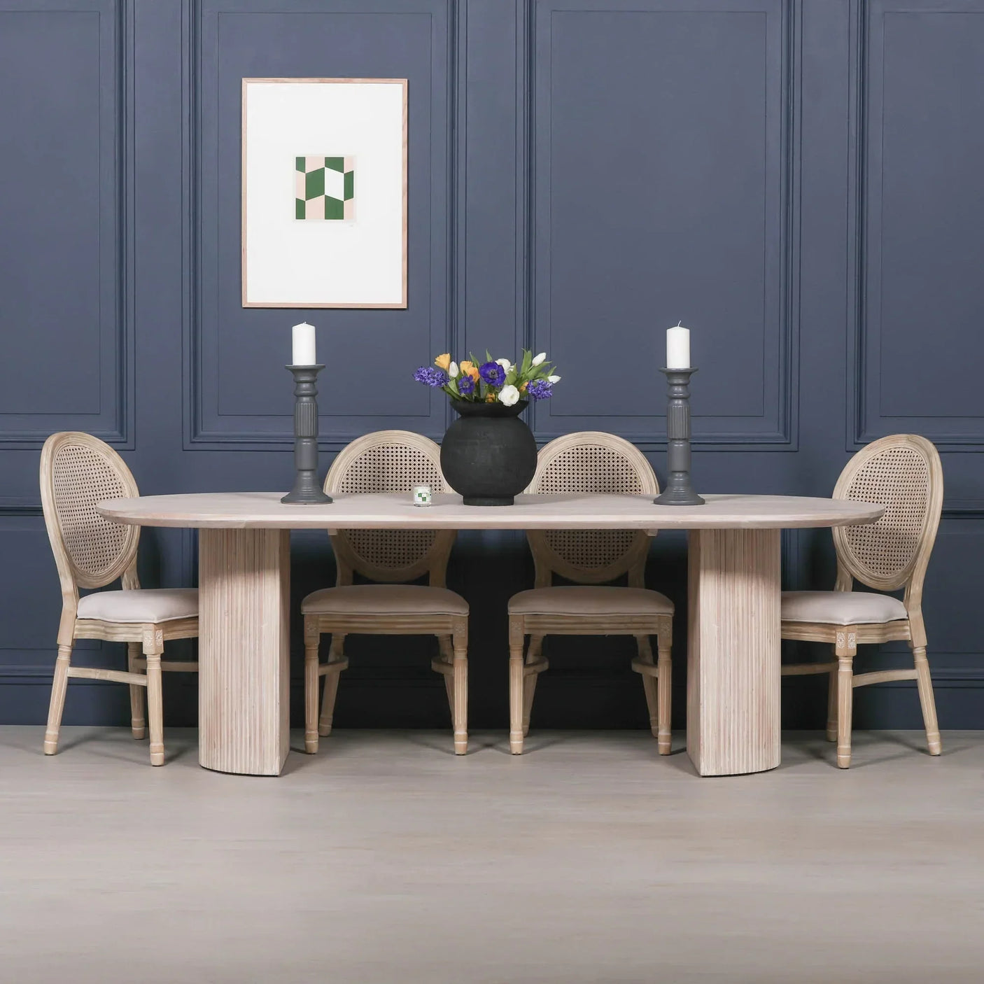 Oval wood dining table with four rattan chairs, black vase, and candles in modern dining room