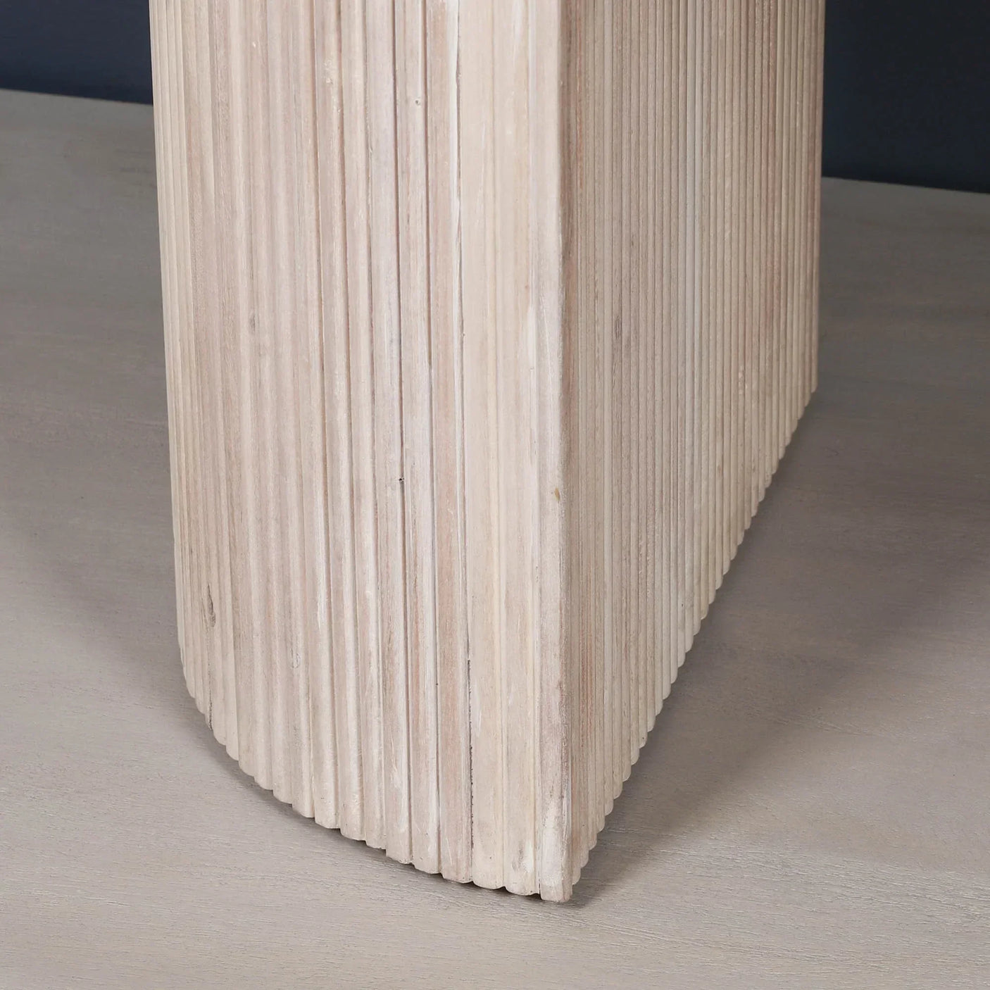 Close-up of ribbed wooden table leg with light finish on pale wood floor