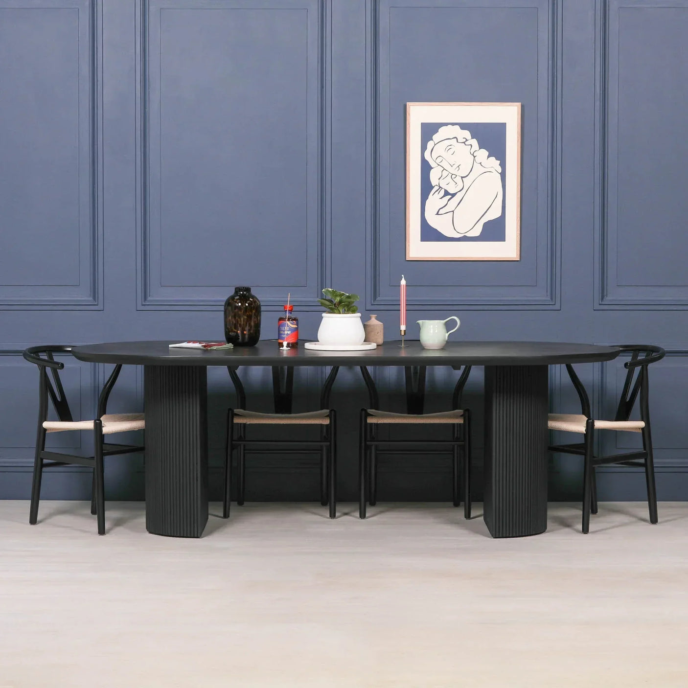 Black dining table with six chairs against blue panel wall, tabletop with decor and art print
