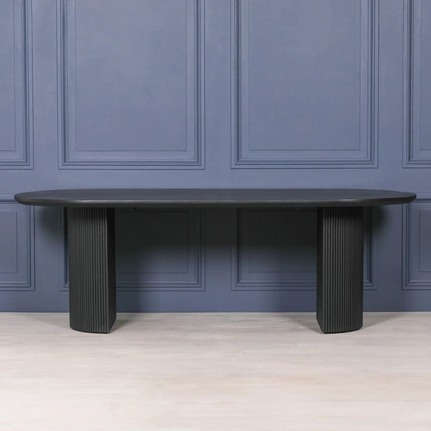 Black dining table with rounded edges and fluted pedestal legs against blue paneled wall