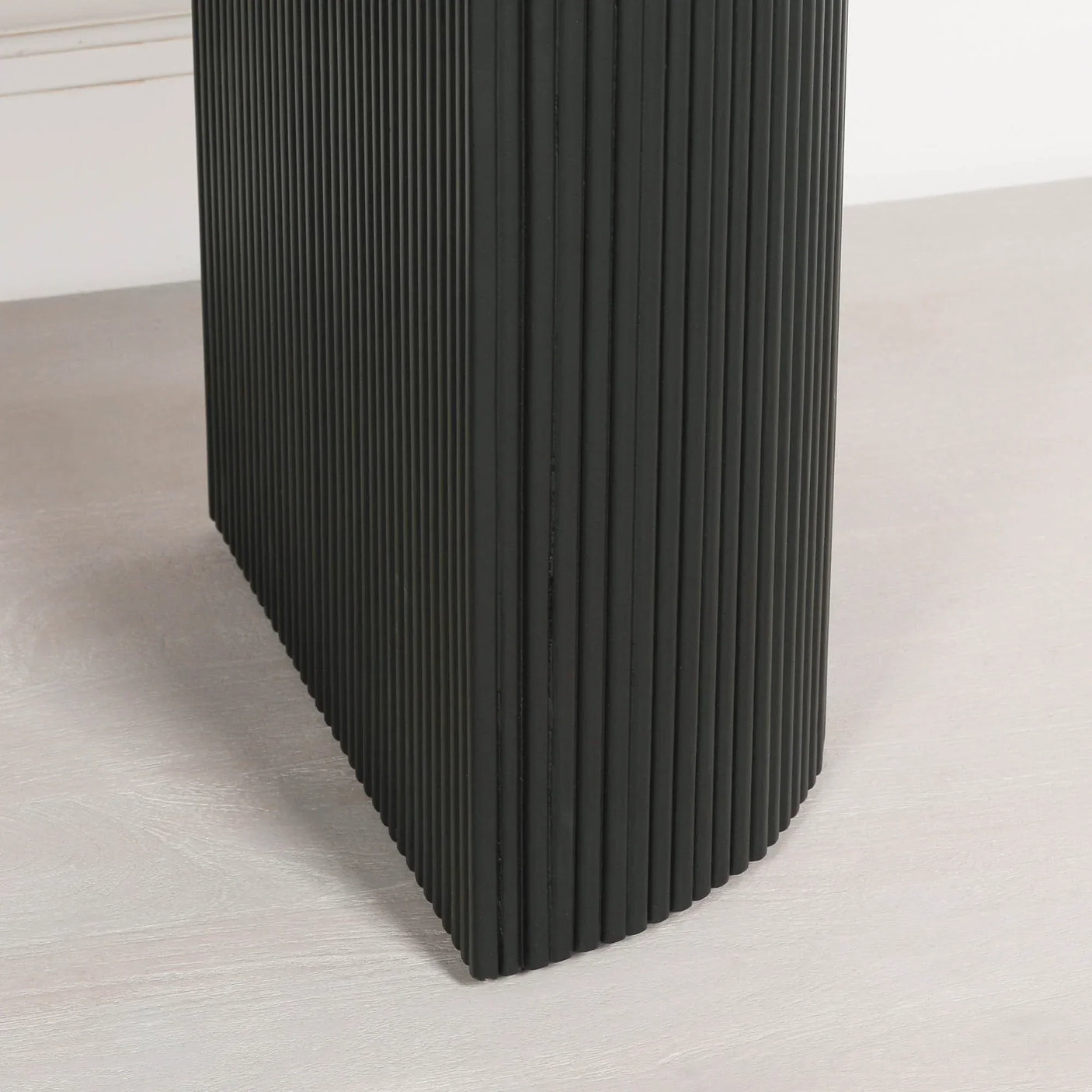 Closeup of black ribbed table leg with curved edge on light wood floor
