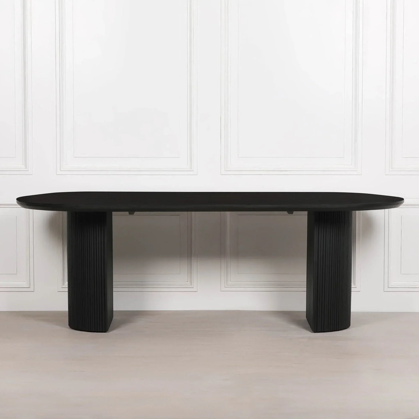 Black wooden dining table with ribbed twin pedestal legs against white panel wall