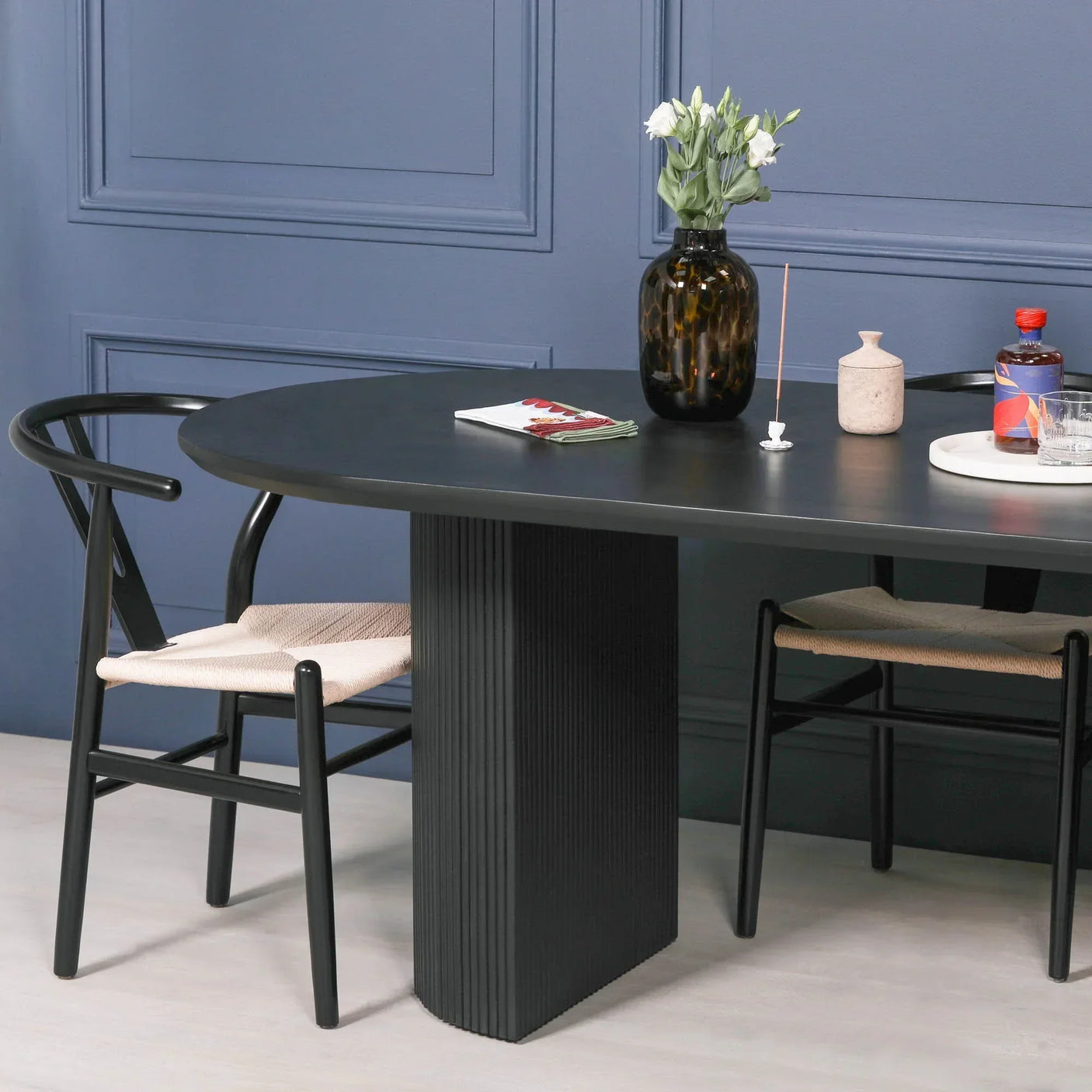 Black oval dining table with ribbed pedestal base and two black dining chairs