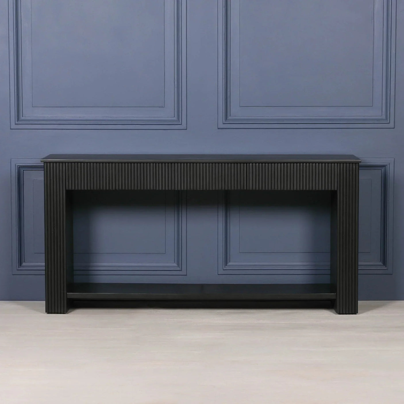 Black wood console table with vertical grooved texture against a blue panel wall