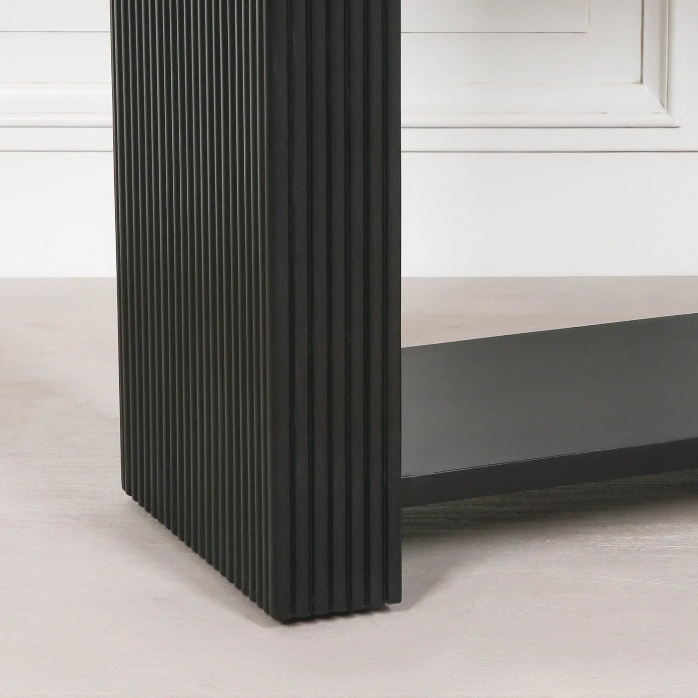 Close-up of black wood coffee table with vertical ribbed leg and lower shelf