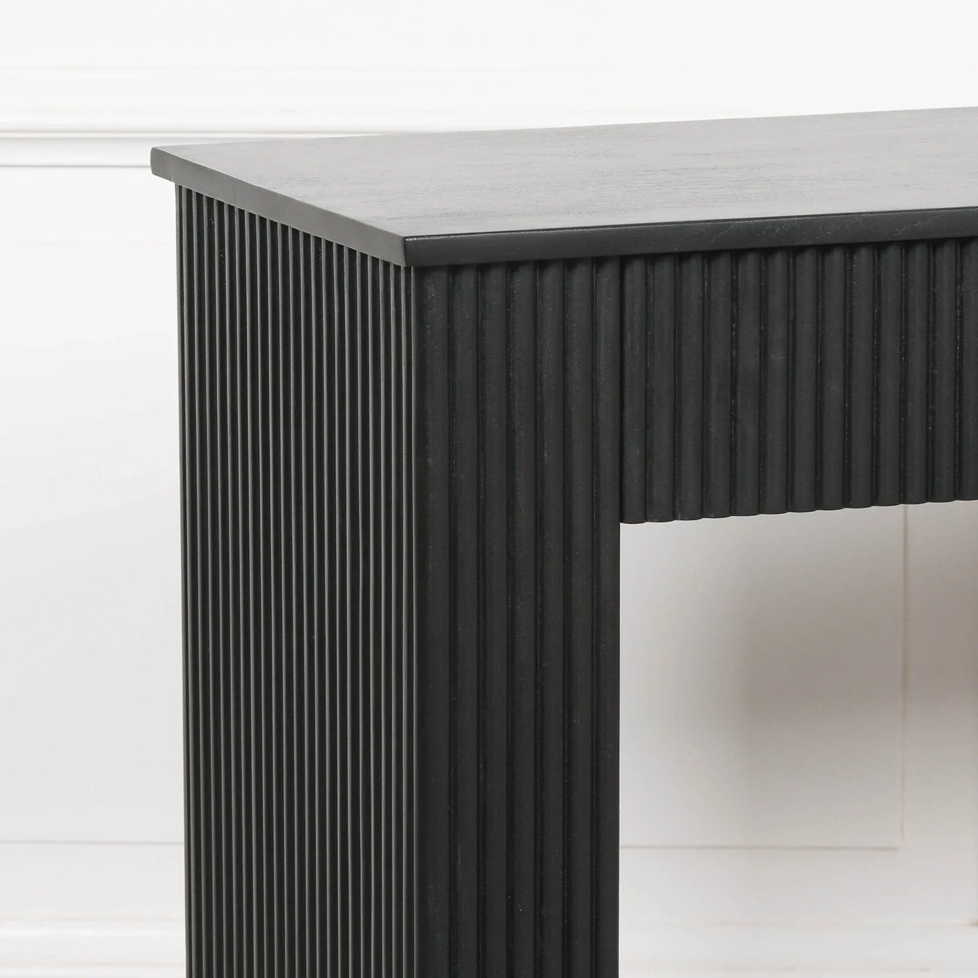 Black console table with vertical ribbed detailing against a white wall