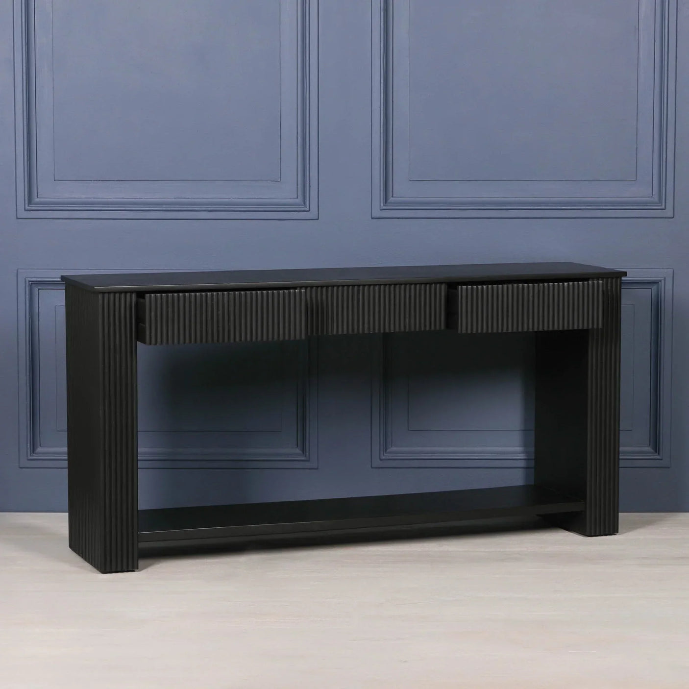 Black wood console table with fluted detail and lower shelf against blue panel wall