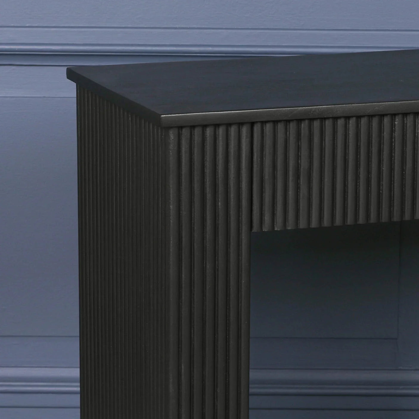 Black wooden console table with fluted front detail against a blue wall