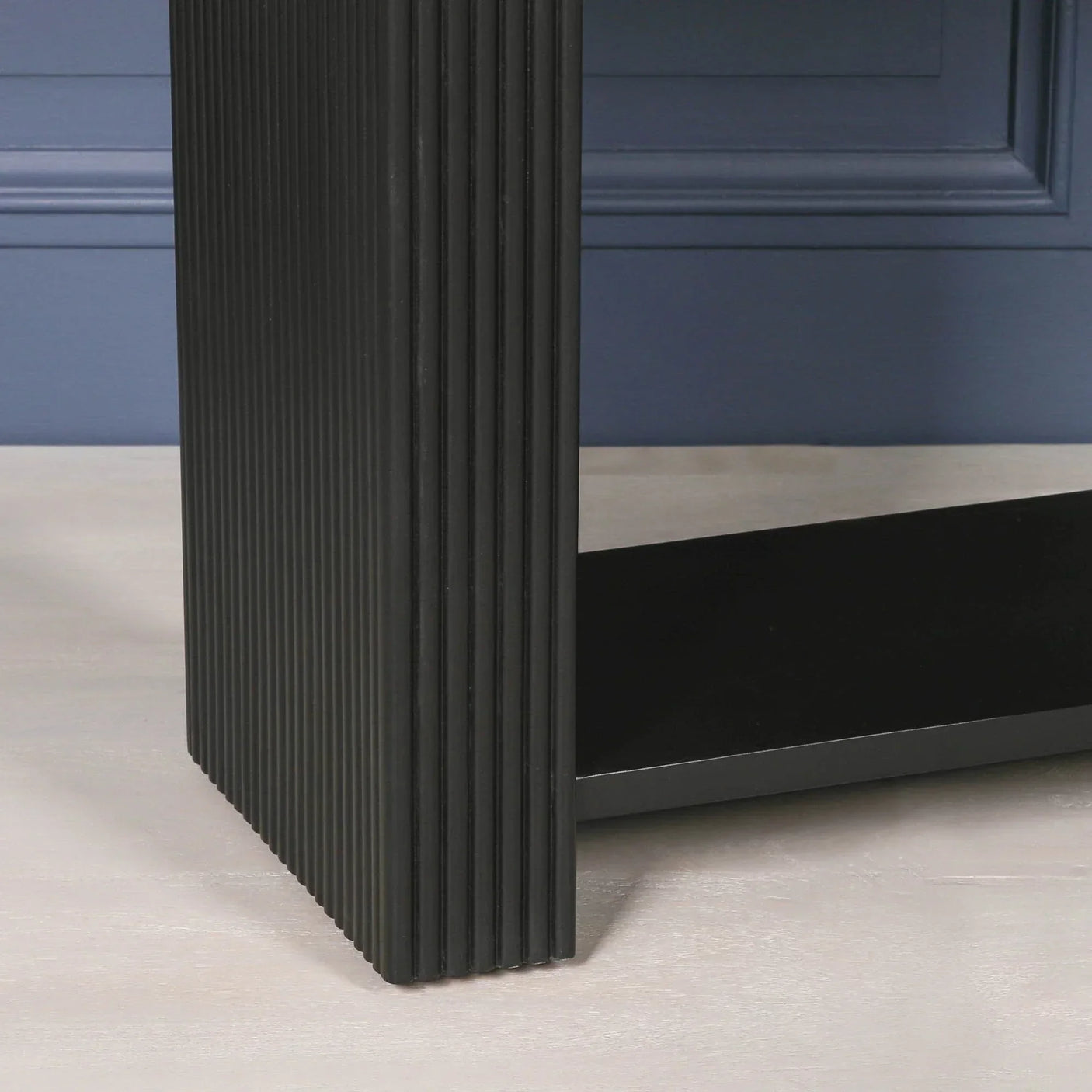Black ridged table leg with matte finish against blue wall and light wood floor