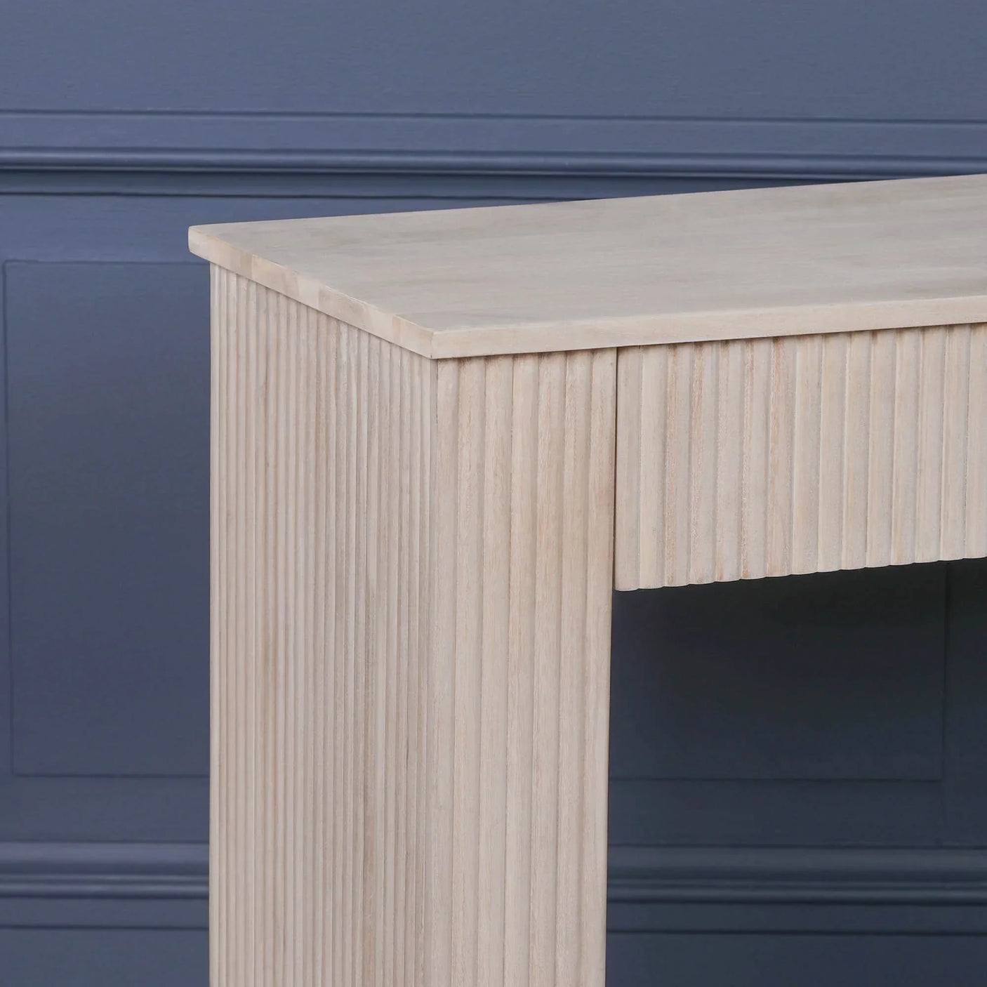 Close up of light wood console table with vertical fluted detail against dark blue wall
