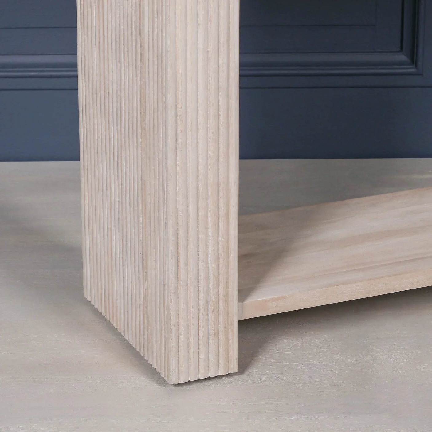 Light wood furniture leg with vertical grooves and lower shelf against blue wall
