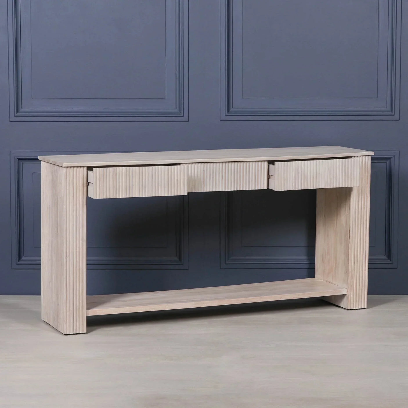Light wood console table with fluted drawer fronts and lower shelf against blue wall