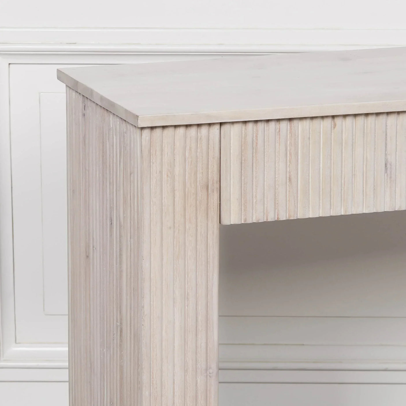 Light wood console table with grooved panel detailing against white wall