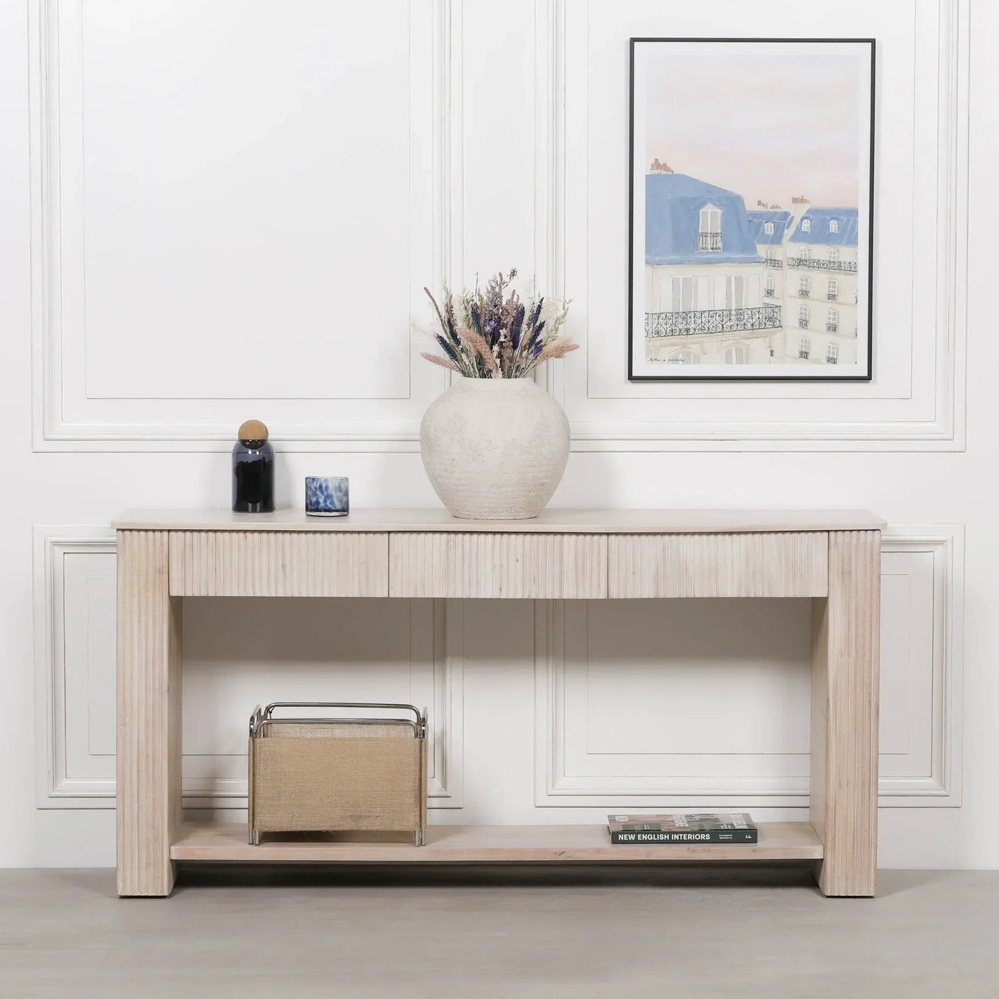 Light wood console table with ribbed finish, vase, decor items, and storage shelf in hallway