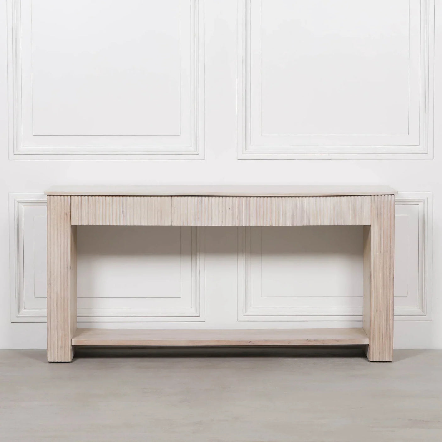 Light wood console table with ribbed detail and lower shelf against white paneled wall