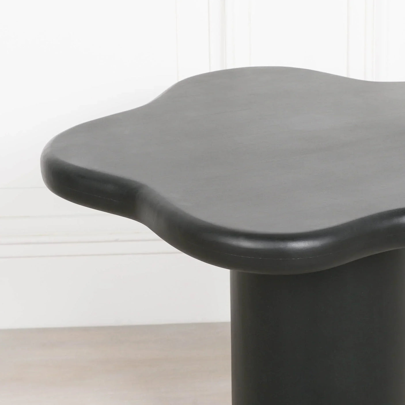 Black modern coffee table with rounded wavy edge and cylindrical base on wood floor