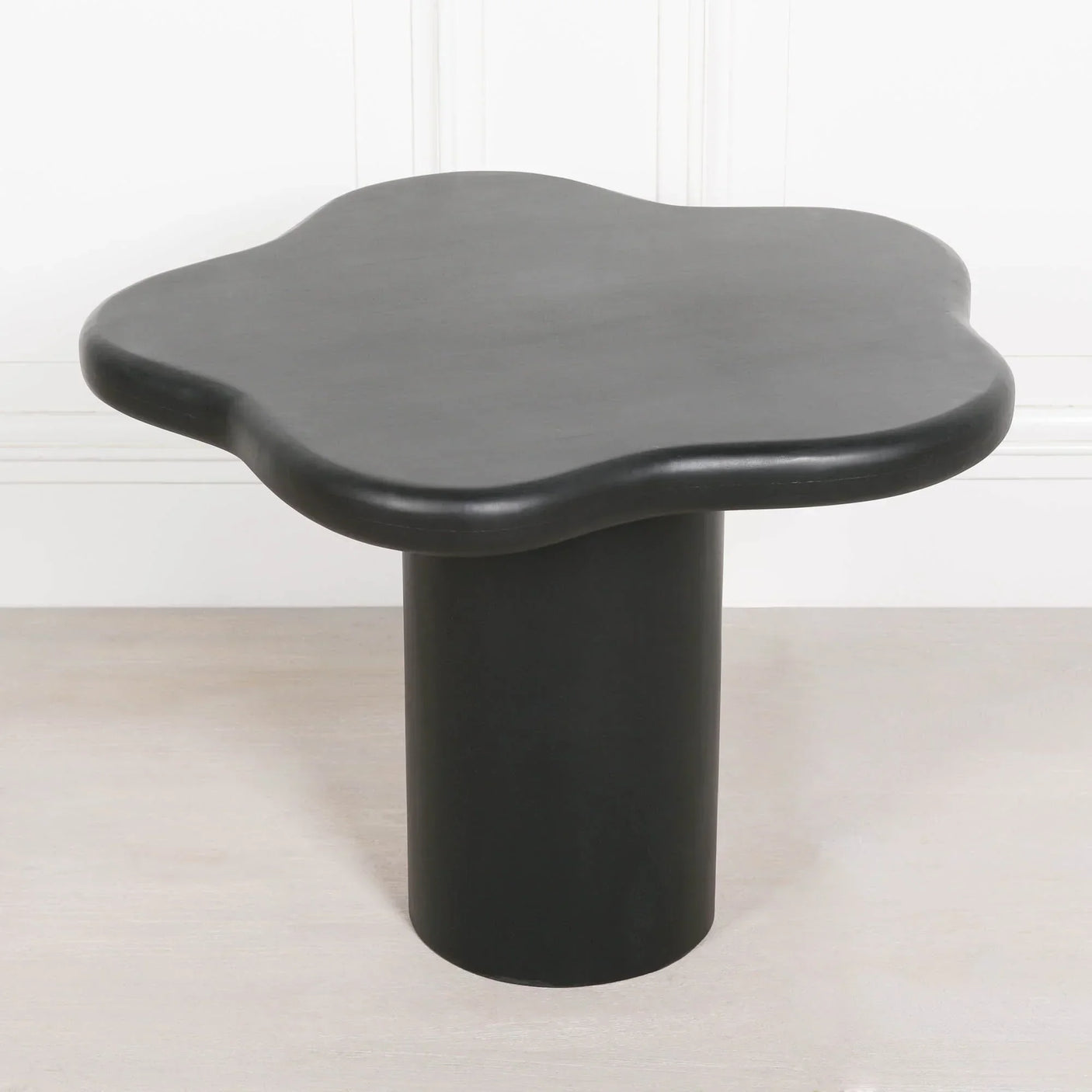Black modern side table with flower-shaped top and cylindrical base on light wood floor