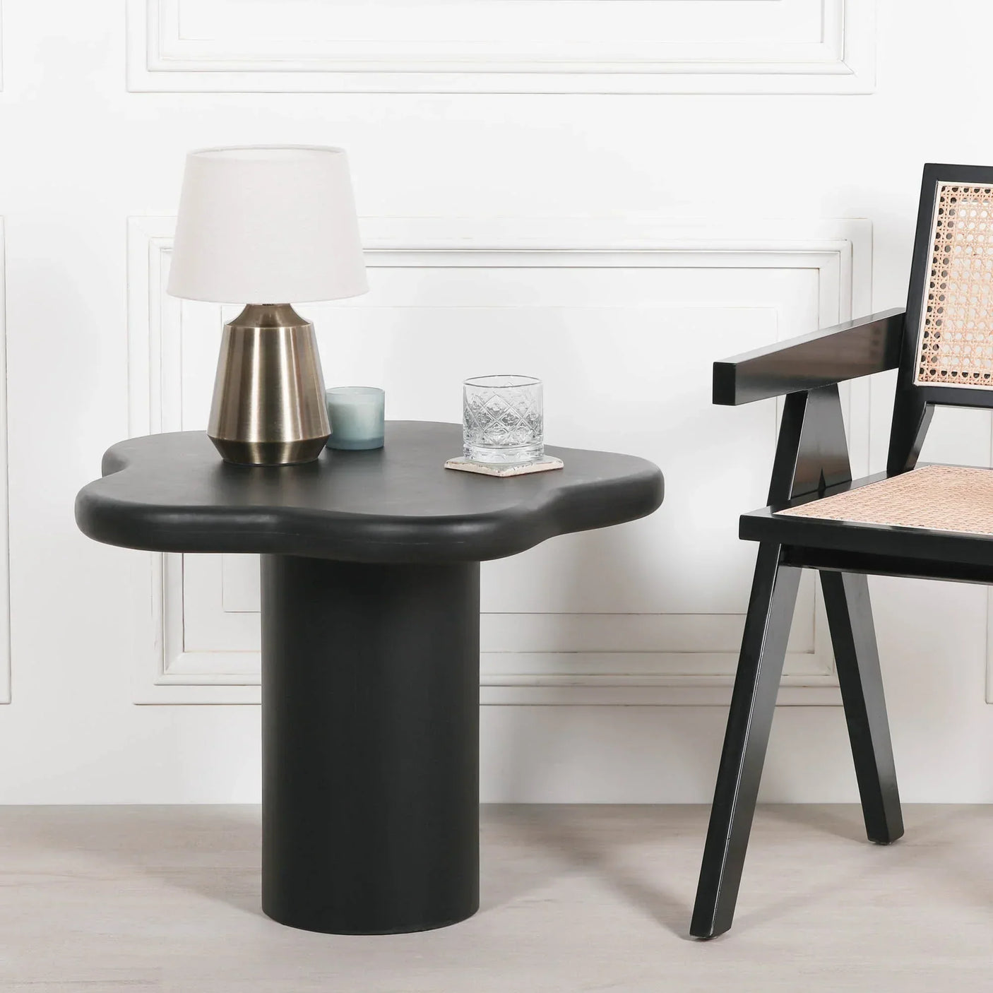 Black modern side table with curved top, lamp, glass, and chair with cane seat