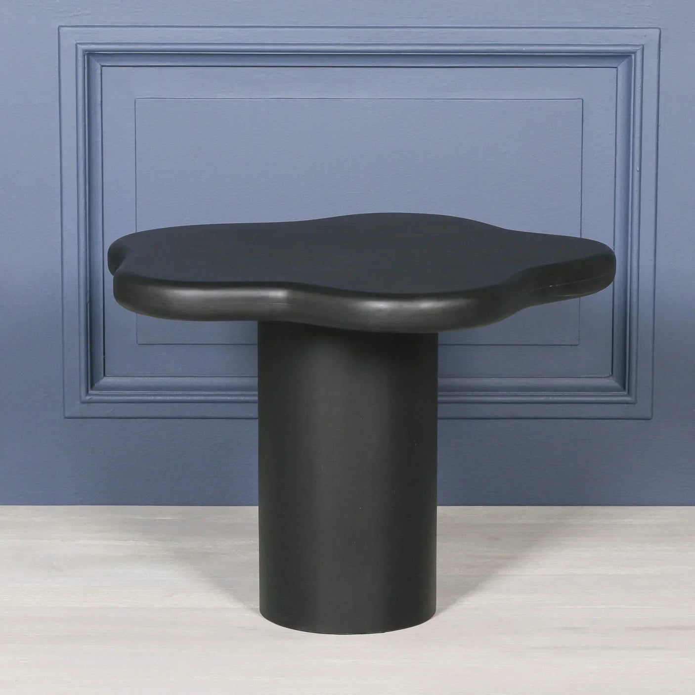 Black modern side table with wavy top and cylindrical base on light wood floor
