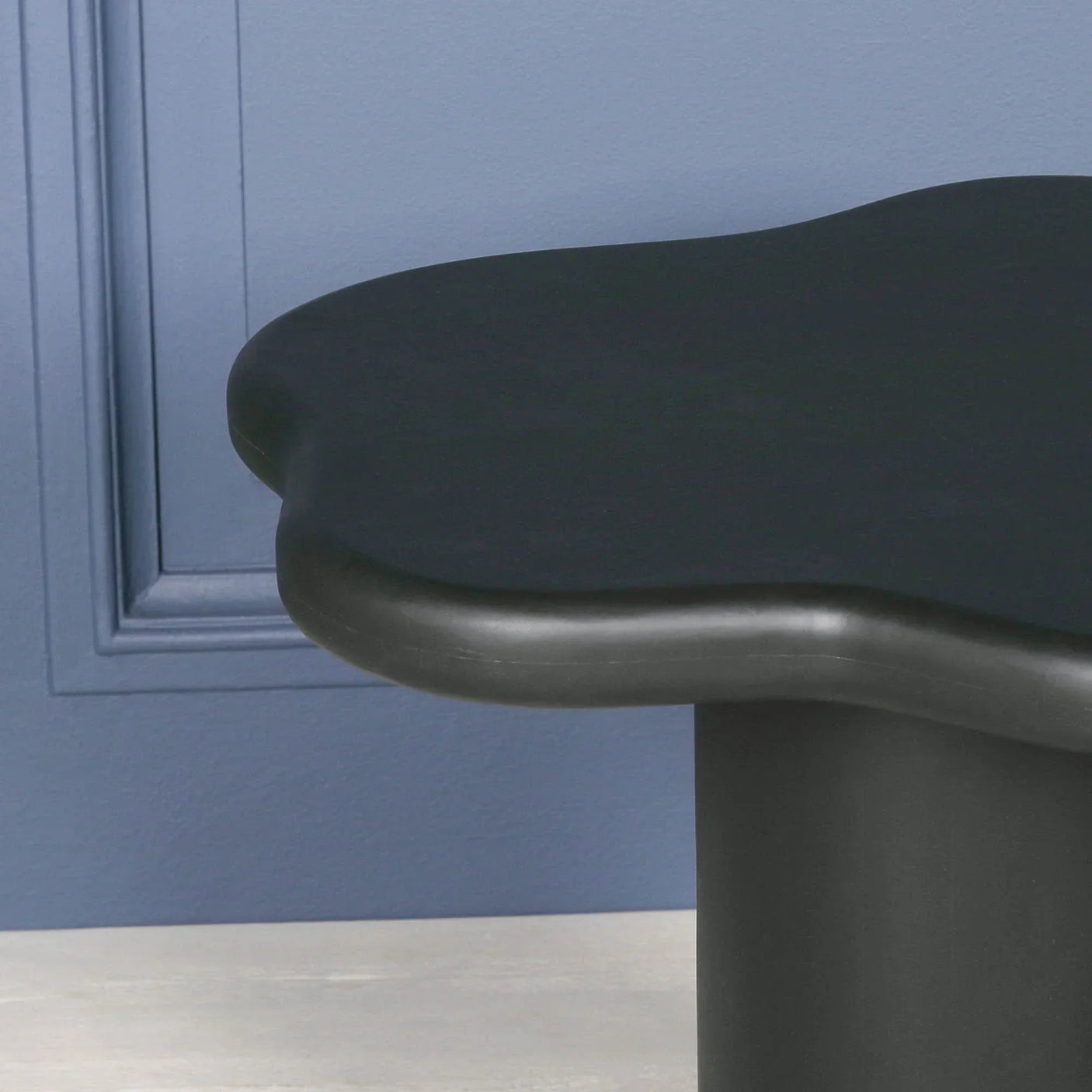 Black coffee table with sculpted edge and rounded base against blue wall
