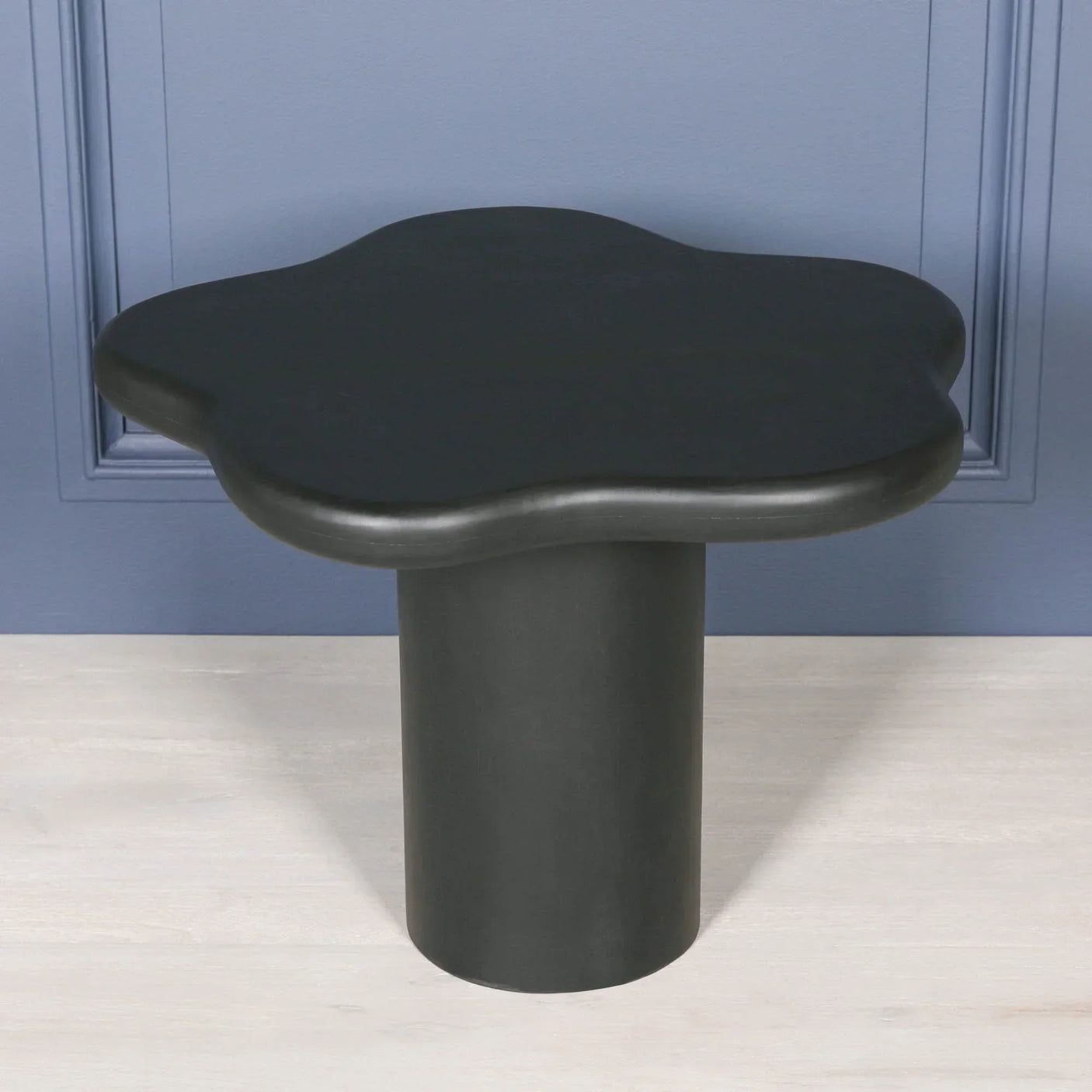 Black side table with cloud-shaped top and cylindrical base against blue wall