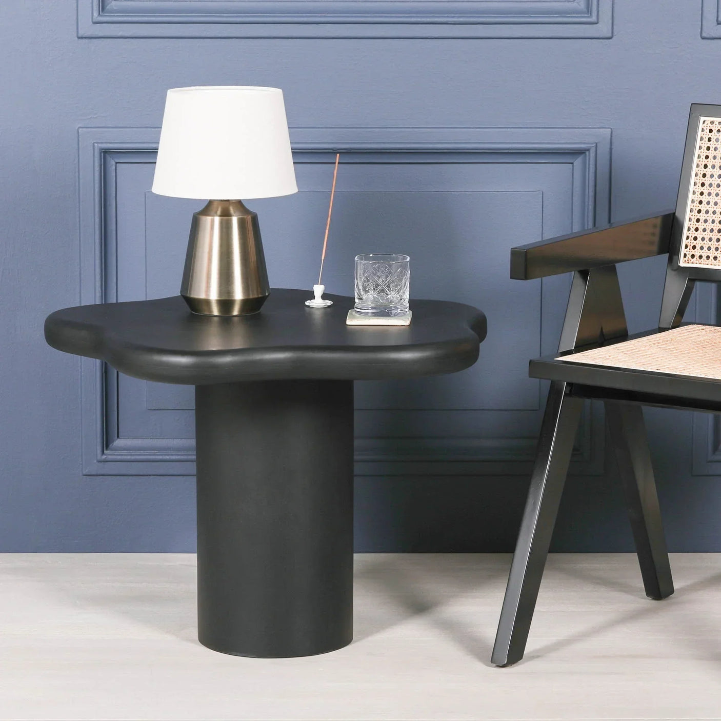 Black modern side table with wavy edge next to black chair and brass table lamp