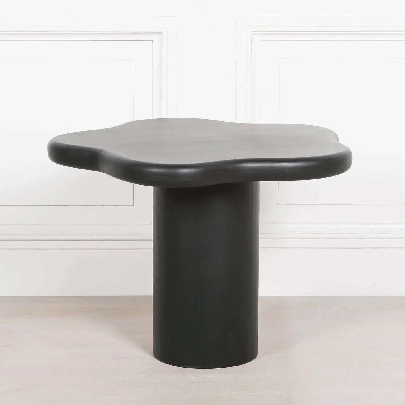 Black modern side table with sculpted top and cylindrical base against white wall