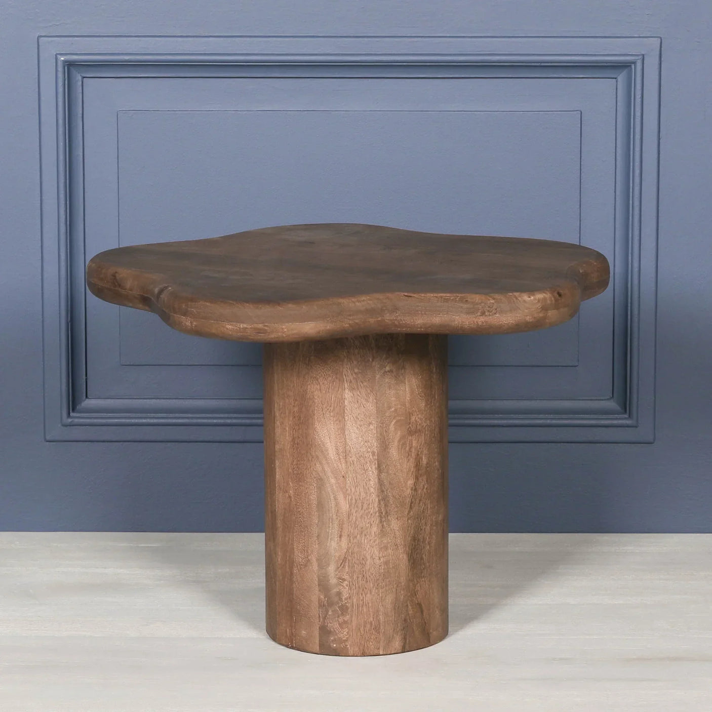 Solid wood coffee table with natural edge top and cylindrical base against blue wall