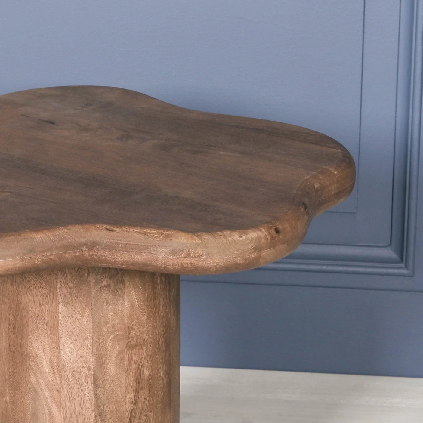 Solid wood coffee table with organic edge and round base against blue wall