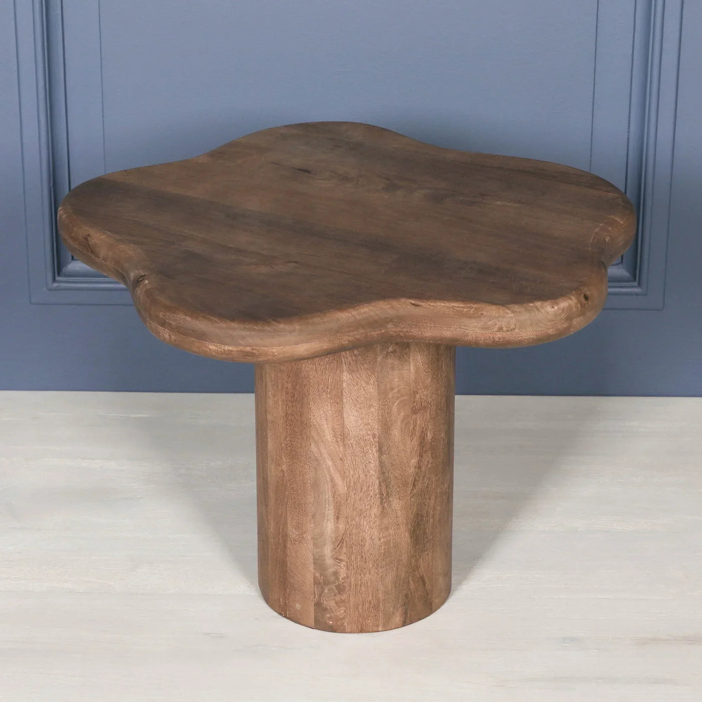 Solid wood coffee table with sculpted top and cylindrical base against blue wall