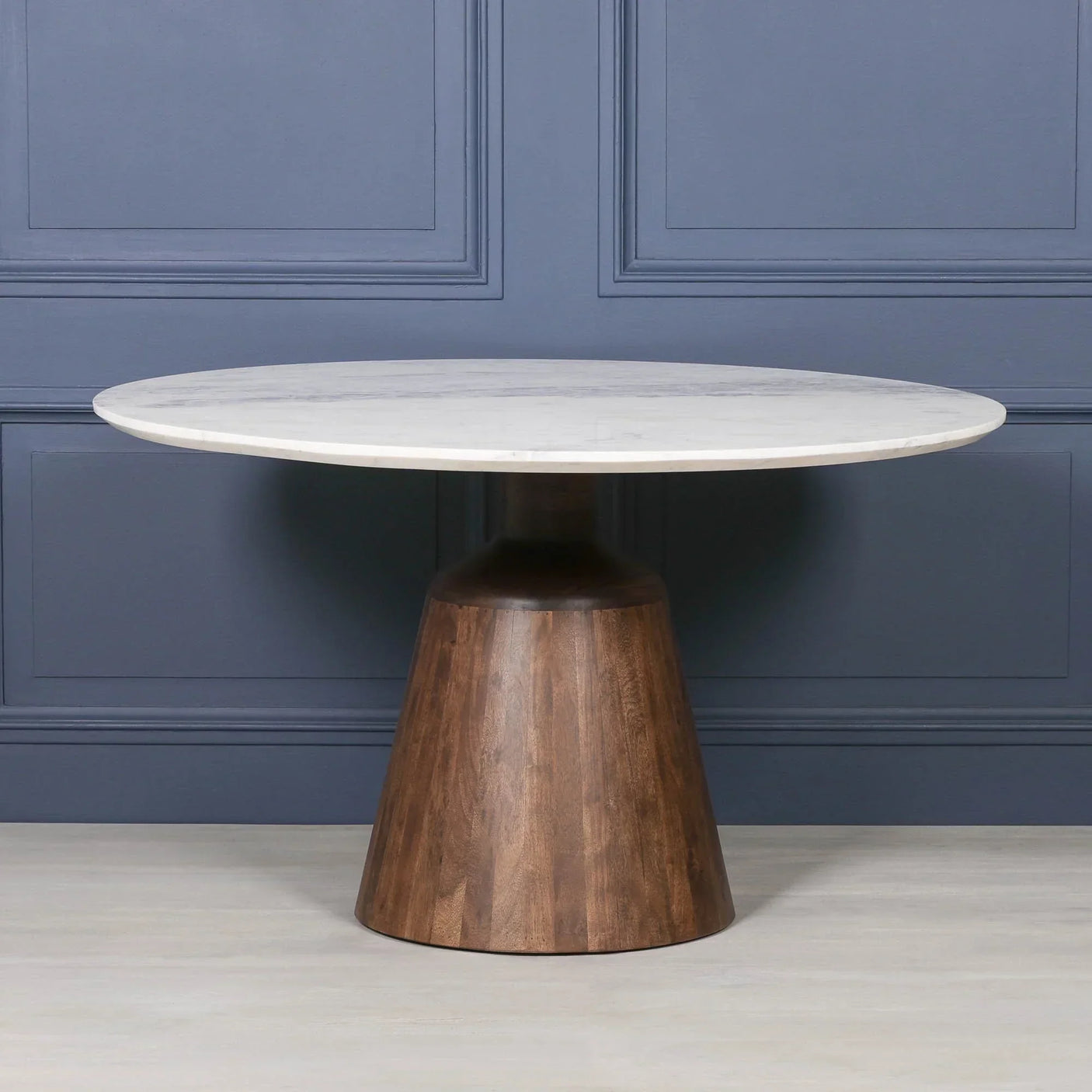 Round marble dining table with wooden pedestal base against blue panelled wall