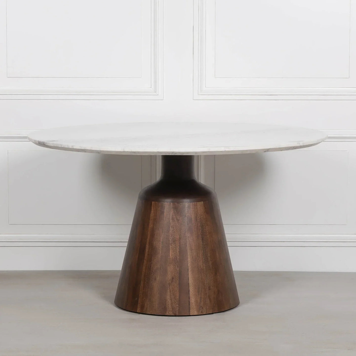 Round dining table with white marble top and cone-shaped dark wood base against white wall